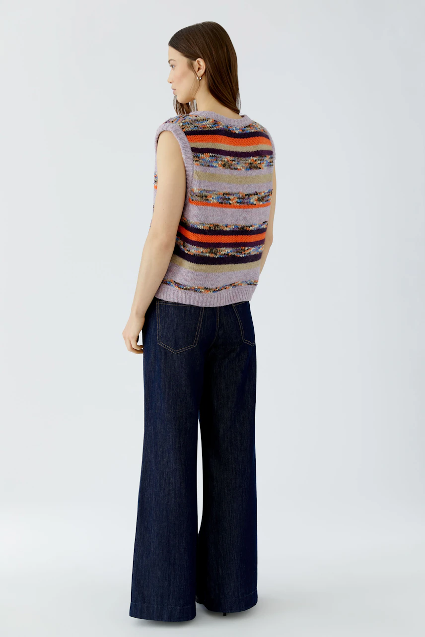 Frau im gestreiften Pullunder und weiter Jeans, seitlich stehend. Lässiger Look für den Alltag.