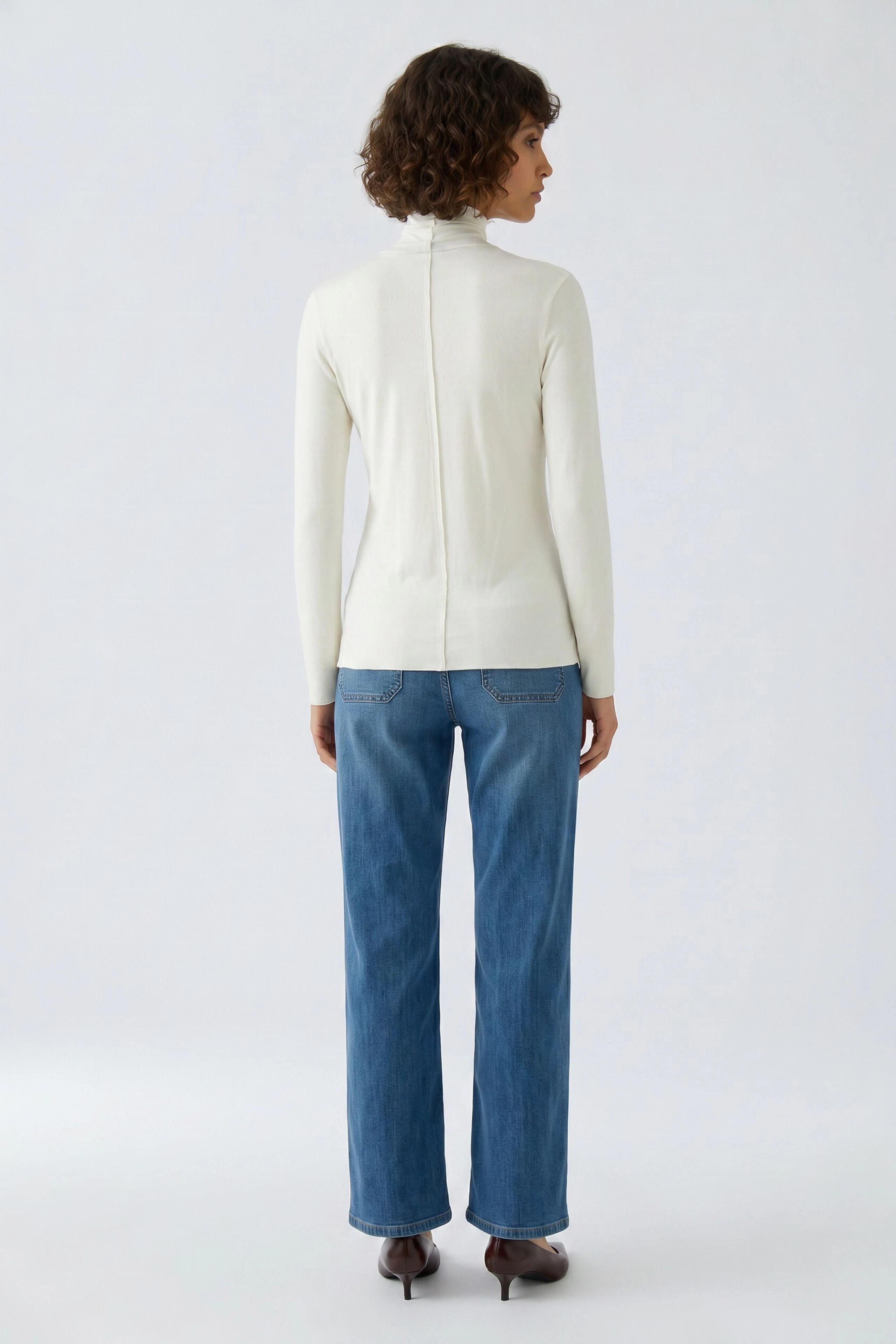 Woman in white long-sleeve shirt and blue jeans, standing confidently. Casual and versatile look.
