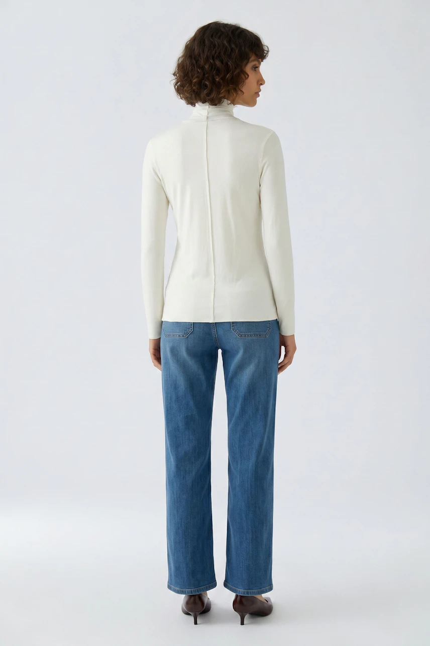 Frau im weißen Langarmshirt und blauer Jeans, von hinten gesehen. Schlichtes Design für lässigen Look.