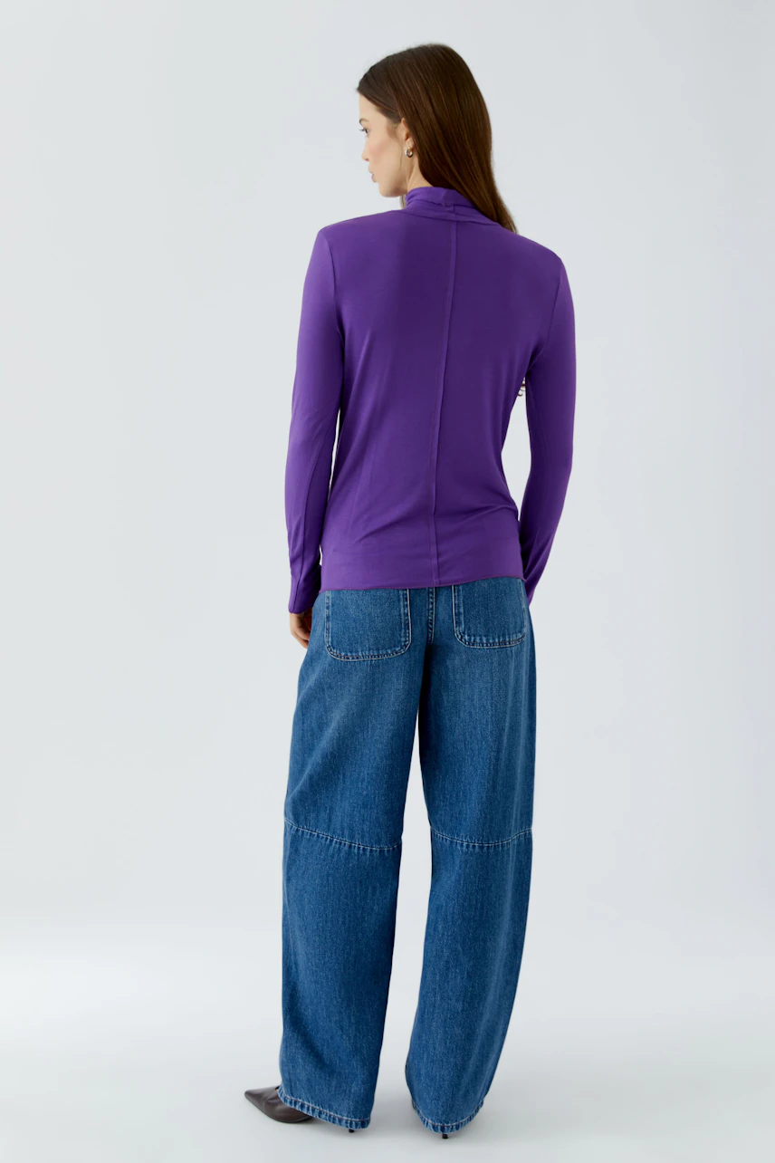 Woman in purple long-sleeve shirt and wide-leg jeans, viewed from the back.
