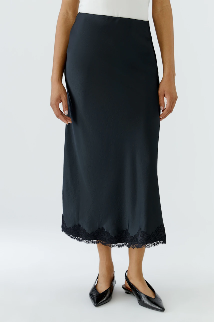 Woman in black maxi skirt with lace hem, white top, and black pointed shoes.