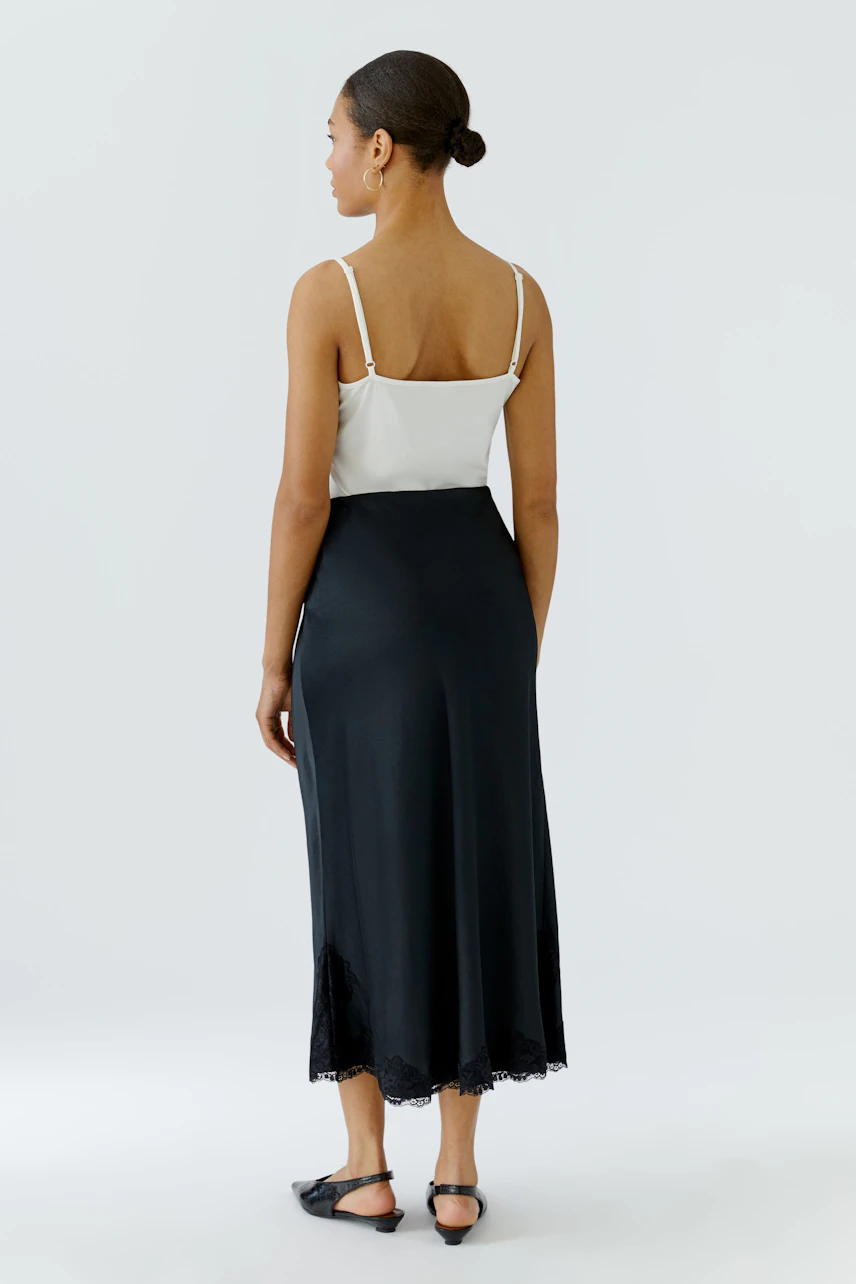 Woman in a black maxi skirt and white top, standing confidently. The skirt flows elegantly to the ankles.