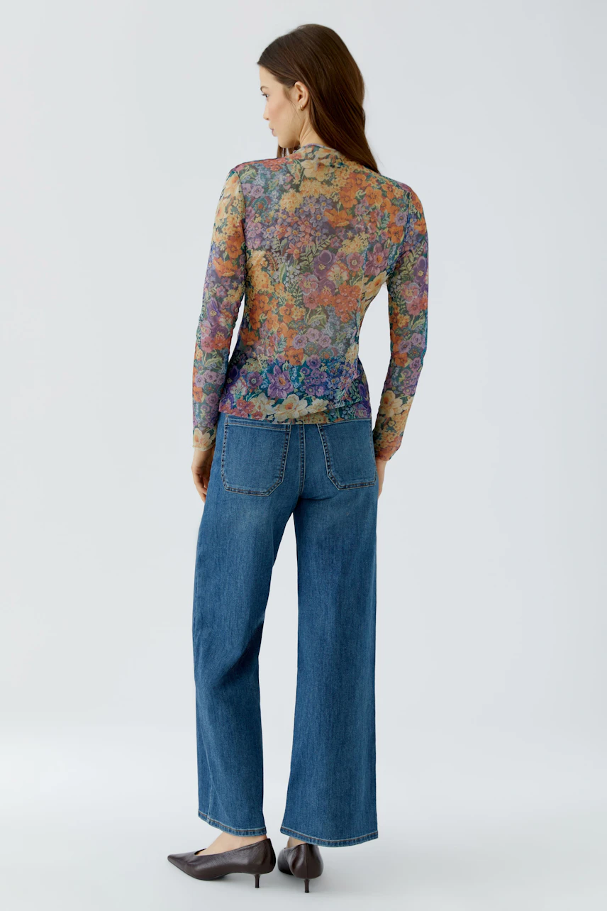 Frau im bunten Langarmshirt und Jeans, von hinten gesehen. Lässiger Look für den Alltag.
