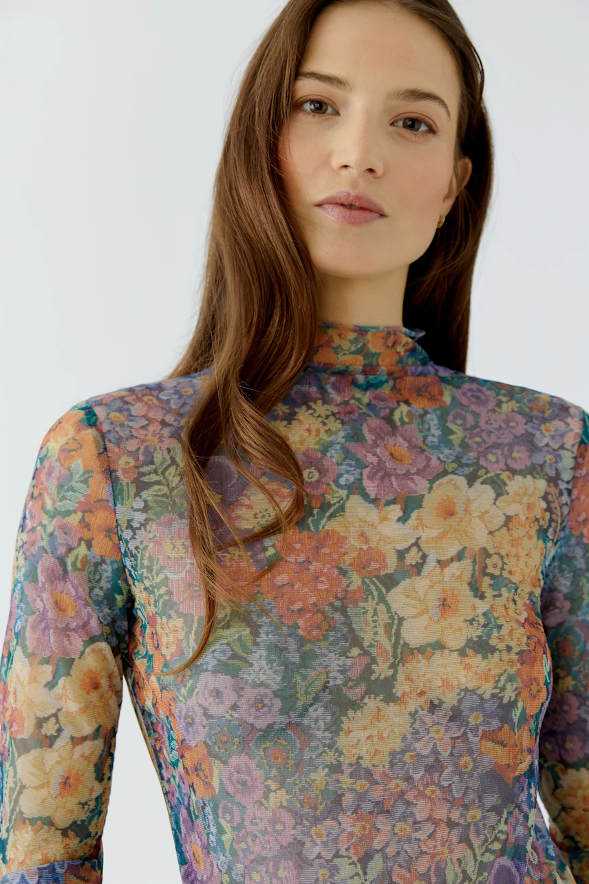 Frau im floralen Langarmshirt: Buntes Muster, schmaler Schnitt, lebendiger Look.