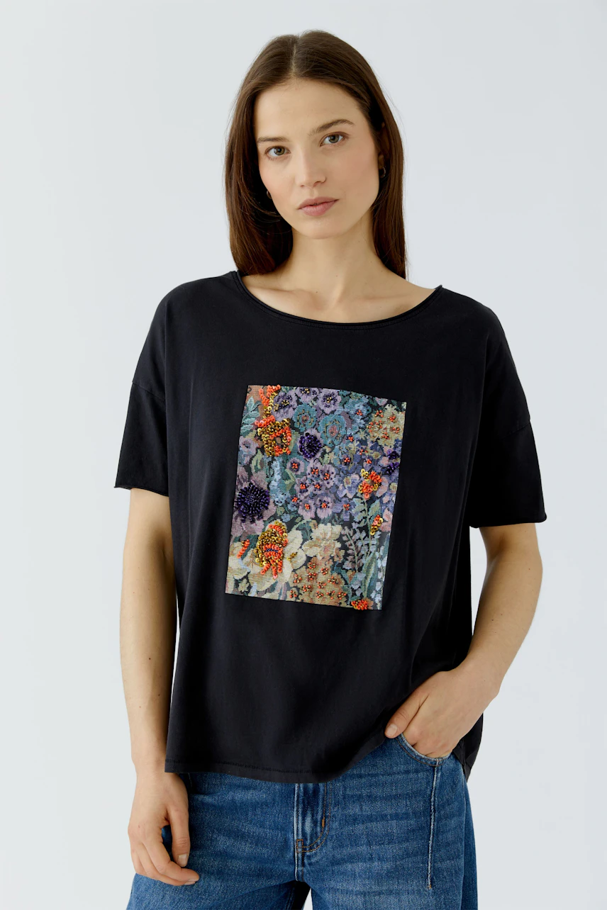 Casual women's T-shirt: Woman in black T-shirt with colorful floral print, paired with blue jeans.