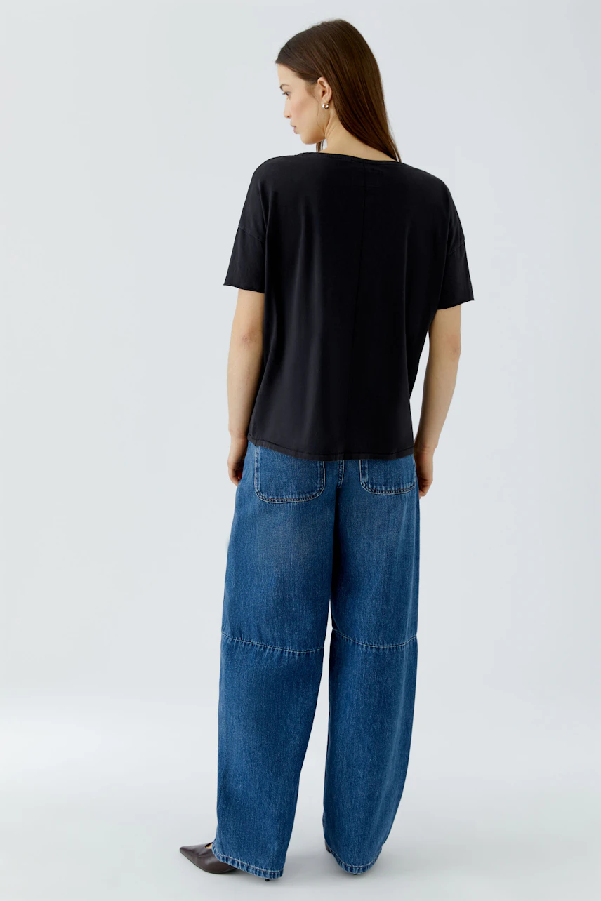 Casual T-shirt: Woman in a black T-shirt and wide blue jeans, viewed from the back.