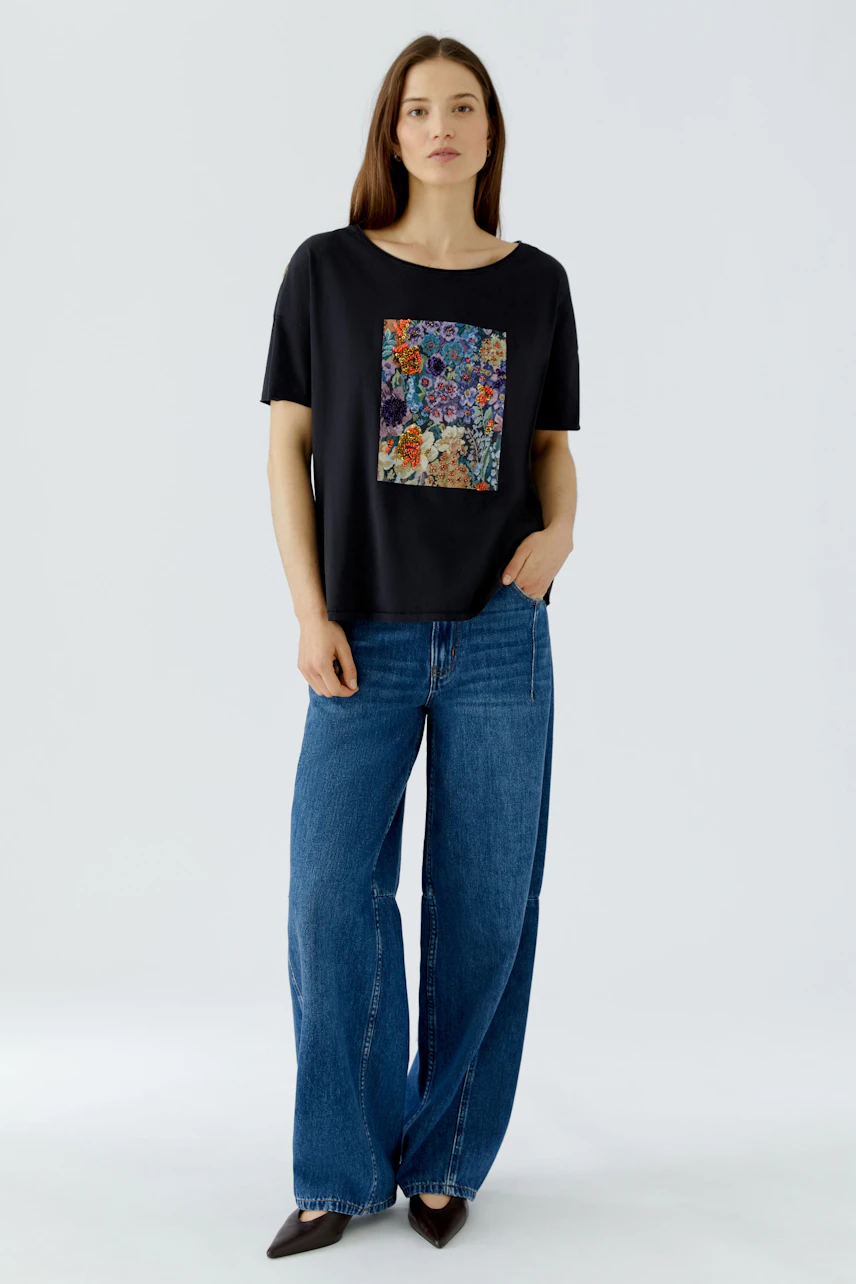 Casual T-shirt: Woman in black T-shirt with colorful floral print, paired with wide-leg jeans, looks relaxed.