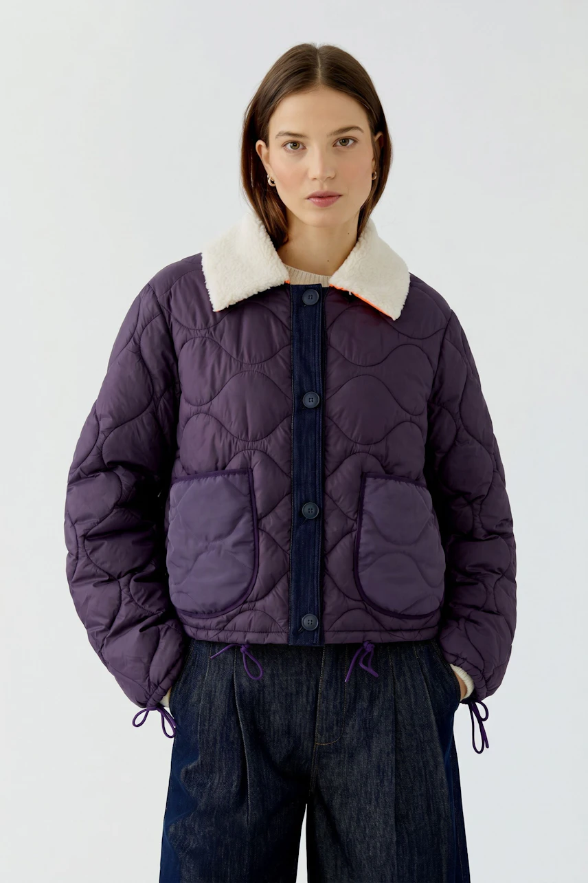 Frau in lila Wendejacke mit hellem Pullover und Jeans. Vielseitig und modern für jeden Anlass.