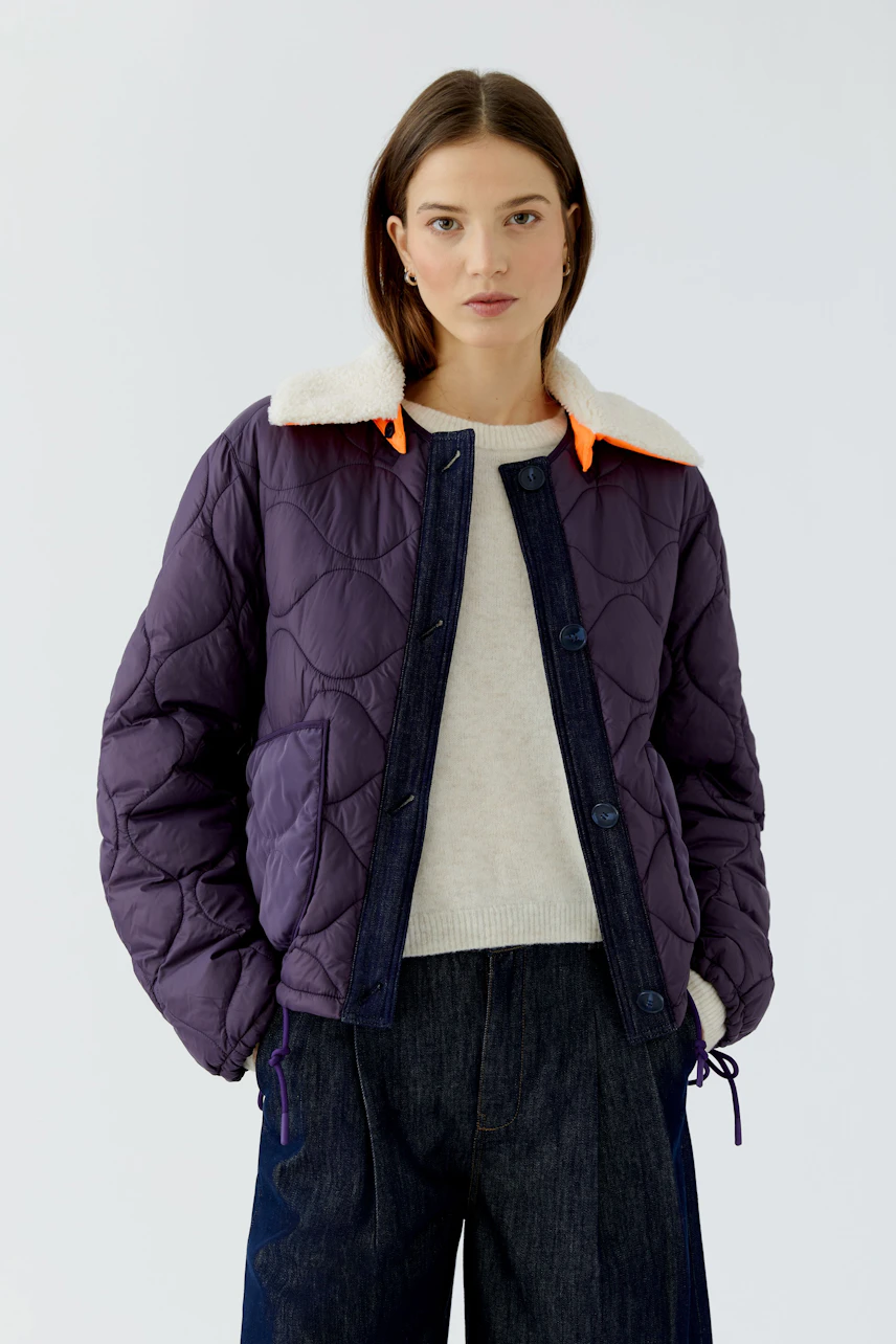 Reversible jacket: Woman in a purple quilted jacket with a cozy white collar and casual denim pants.