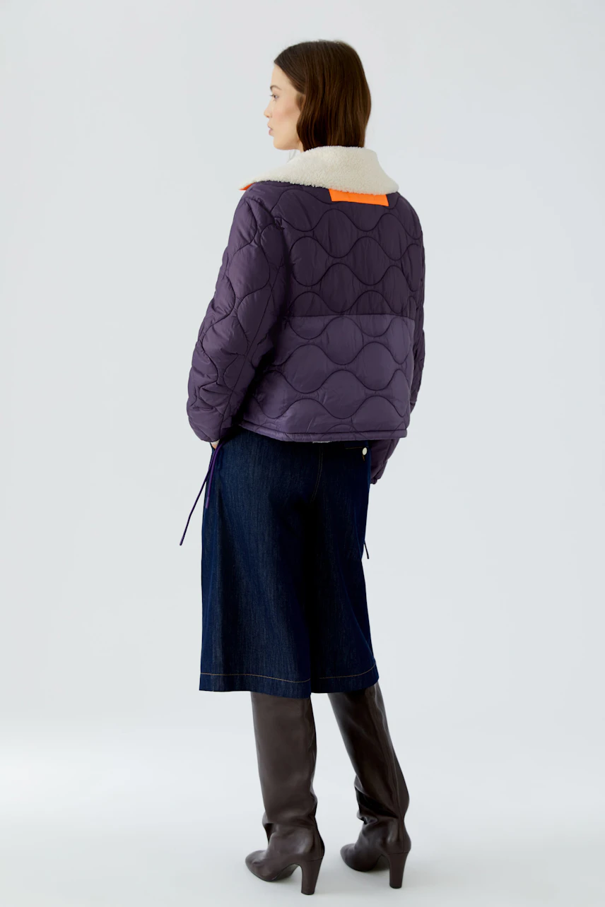 Reversible jacket: Woman in a quilted purple jacket with shearling collar, denim skirt, and knee-high boots.