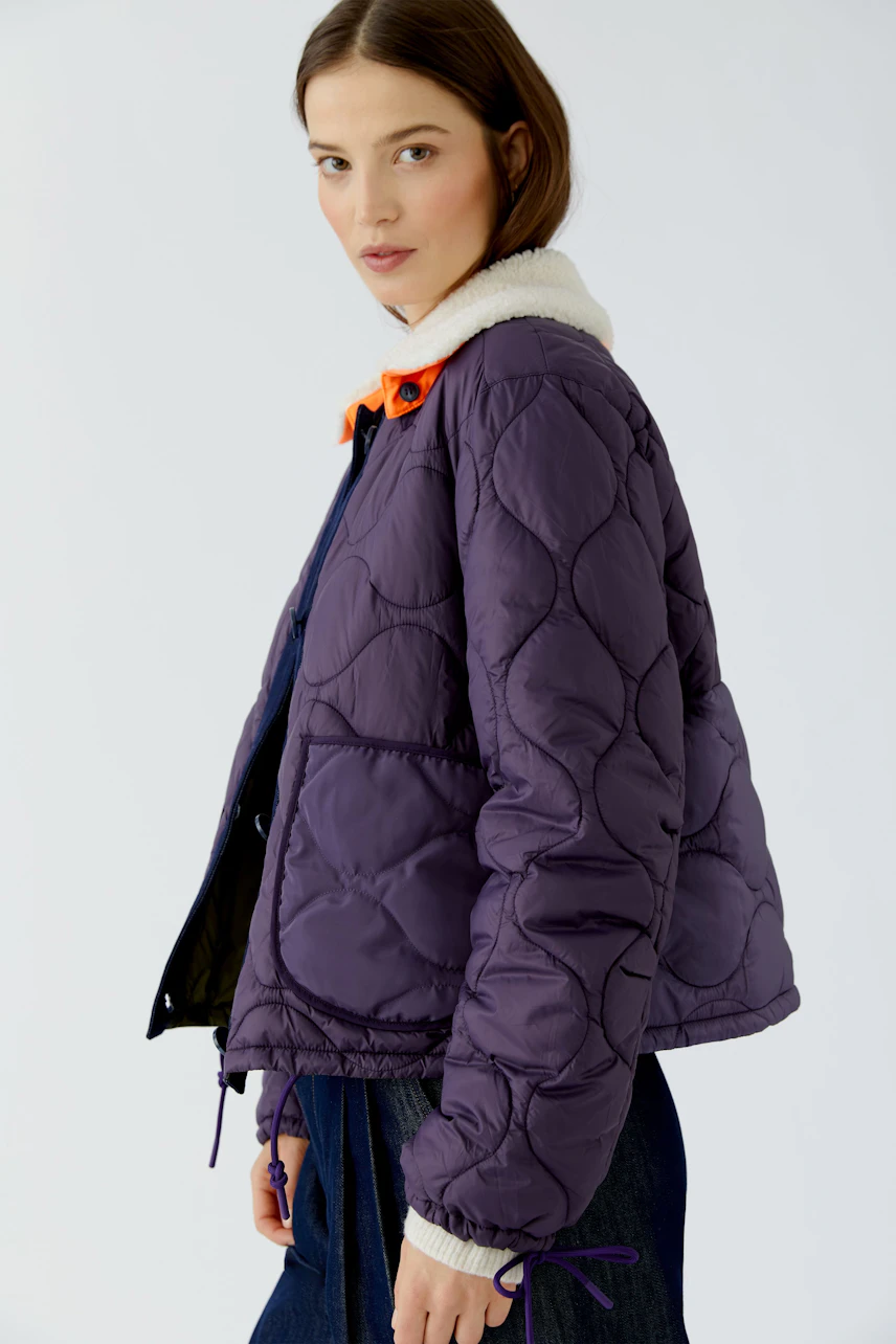 Reversible jacket: Woman in a quilted purple jacket with a cozy collar, paired with casual denim.