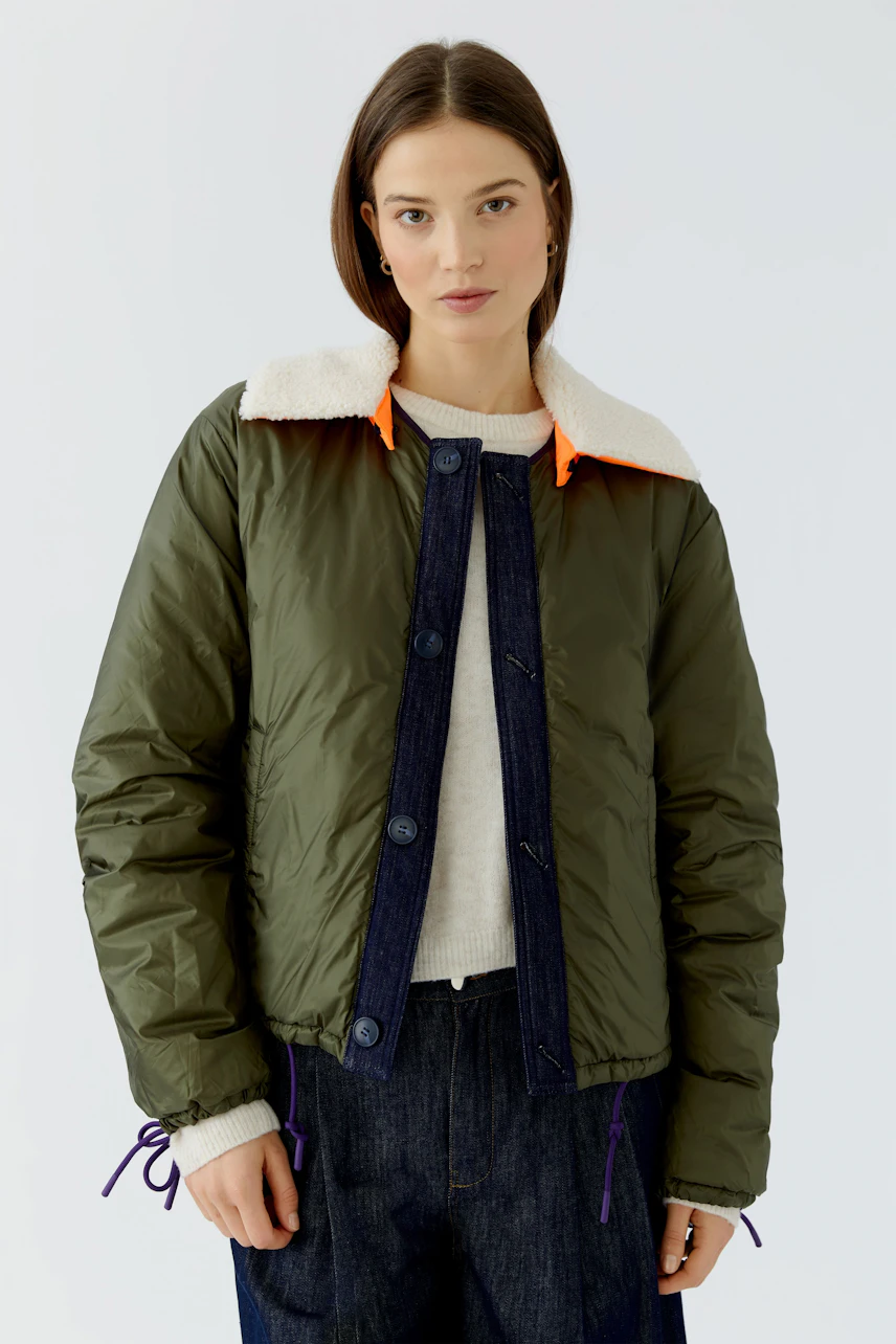 Reversible jacket: Woman in green jacket with white collar, casual style, paired with denim and pullover.