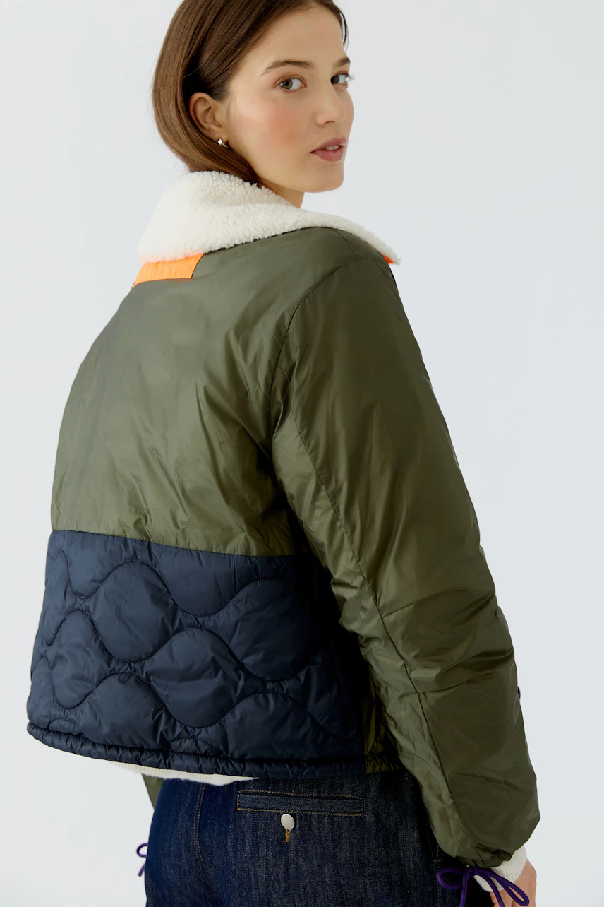 Reversible jacket: Woman in green and navy quilted jacket with white collar, looking over her shoulder.