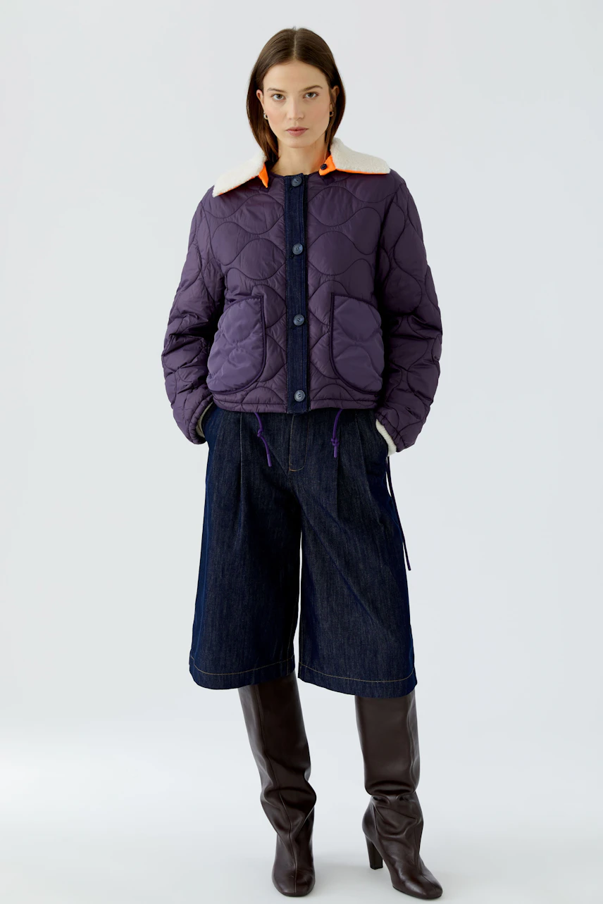 Reversible jacket: Woman in quilted purple jacket with white collar, denim culottes, and knee-high boots.
