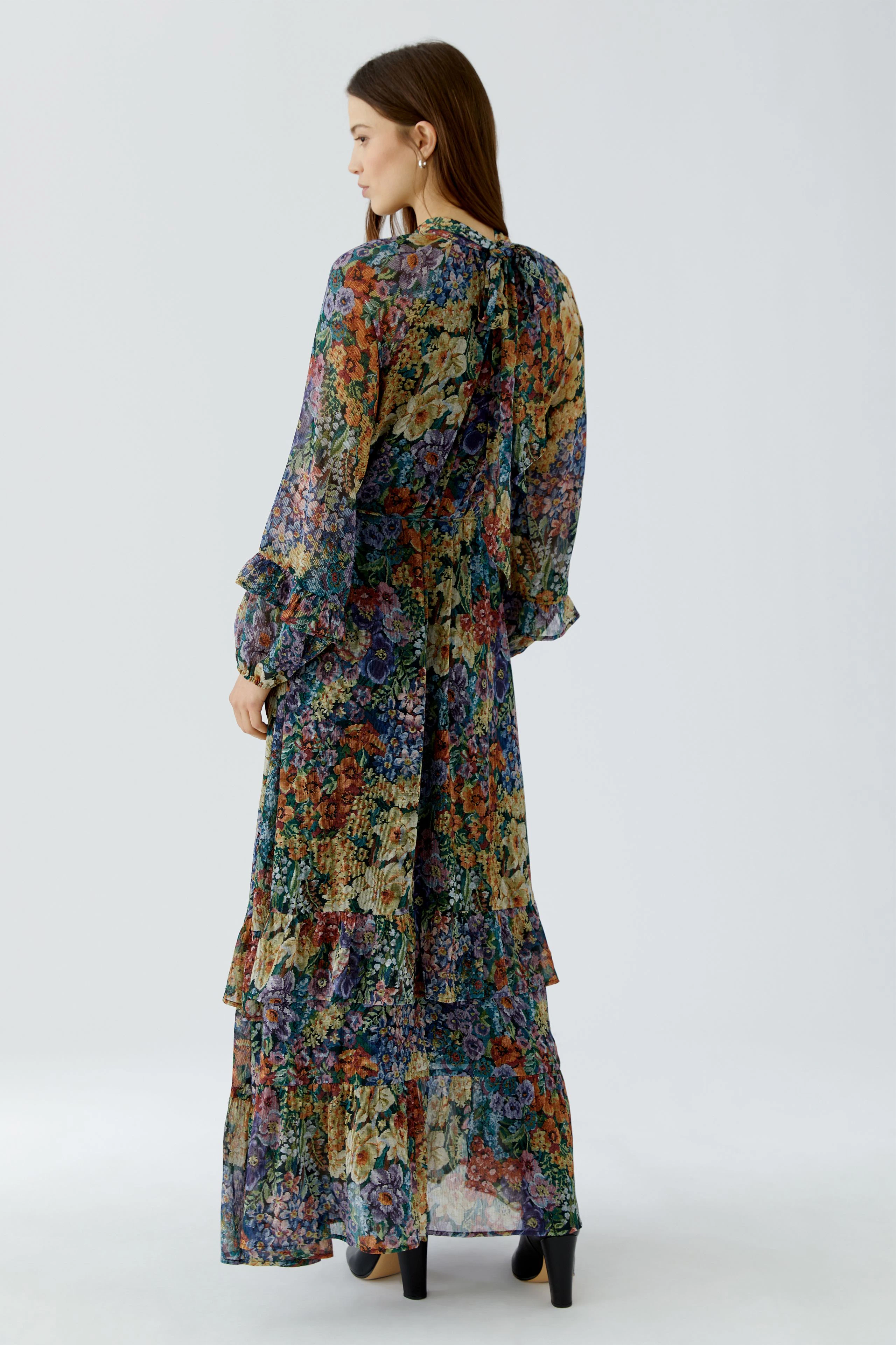 Frau im floralen Maxikleid: Langes, buntes Kleid mit Rüschenärmeln und Stufenrock, Rückansicht.