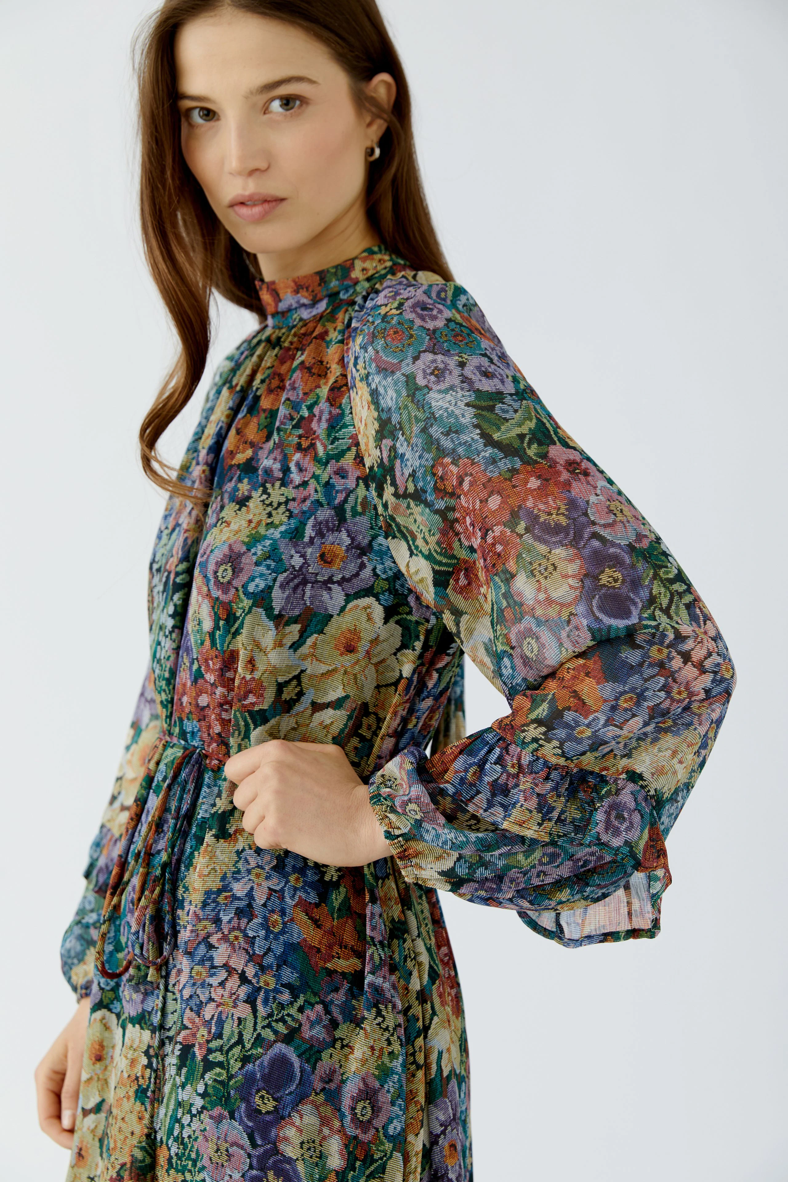 Frau im floralen Maxikleid mit langen Ärmeln und lebendigem Muster, schaut selbstbewusst zur Seite.