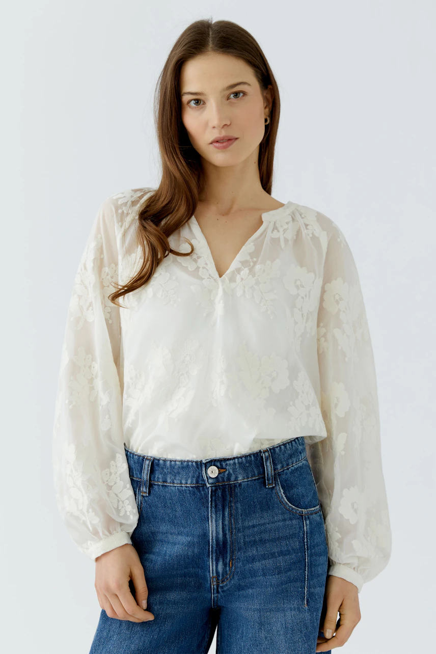 Casual tunic: Woman in a white floral tunic with sheer sleeves and blue jeans, looking relaxed.