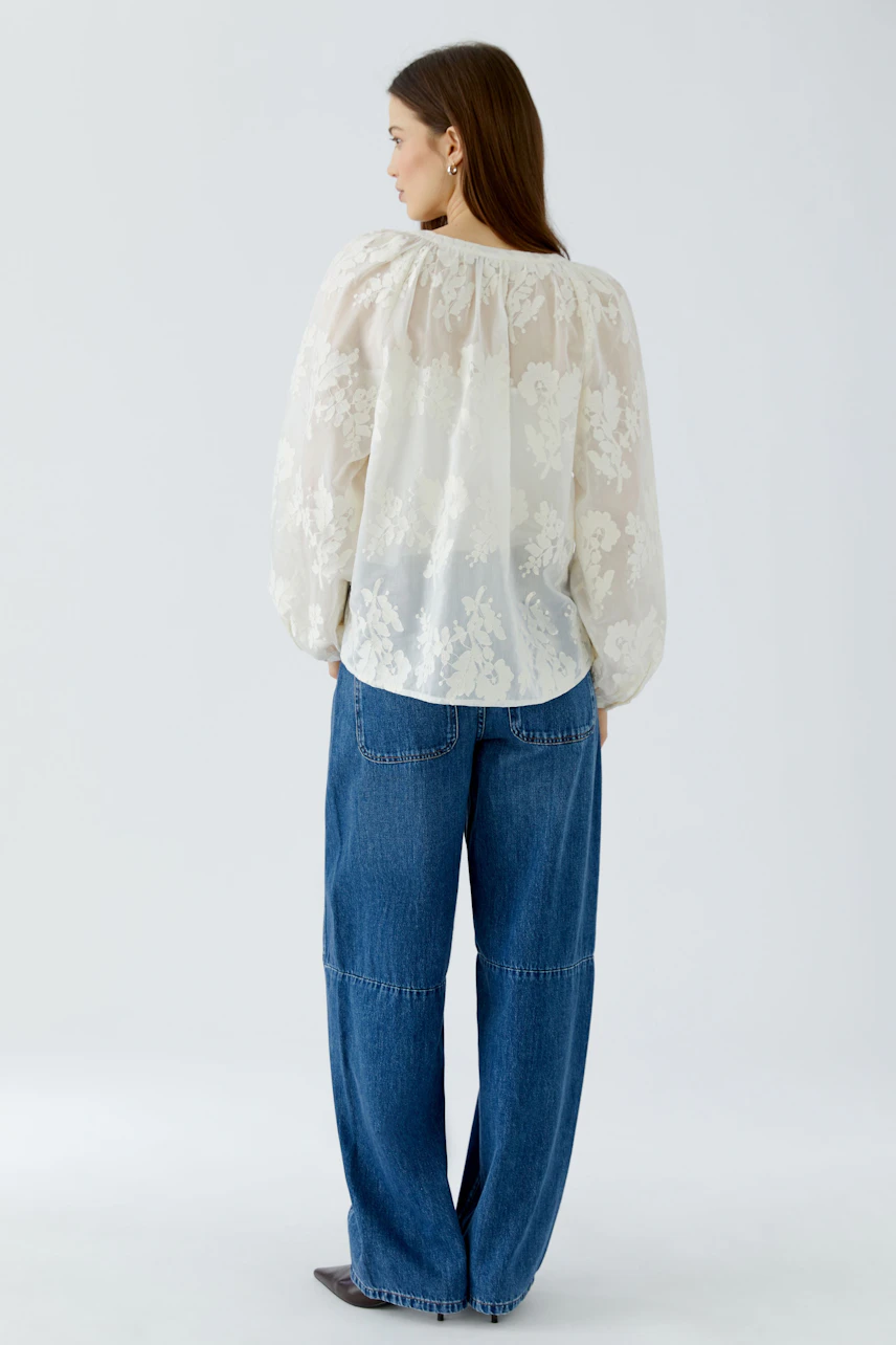 Woman in a sheer floral tunic and wide-leg jeans, viewed from the back.