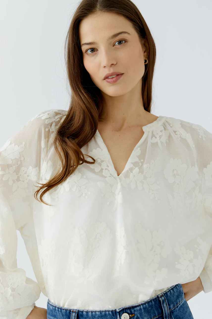 Casual tunic: Woman in a white floral tunic with sheer sleeves, paired with blue jeans, looking relaxed.