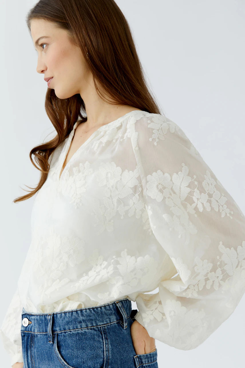 White floral tunic: Woman in a flowy, embroidered tunic paired with blue jeans, side profile view.