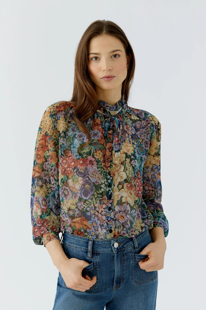 Florale Damen-Bluse: Frau in bunter Bluse mit Blumenmuster und blauer Jeans schaut selbstbewusst.
