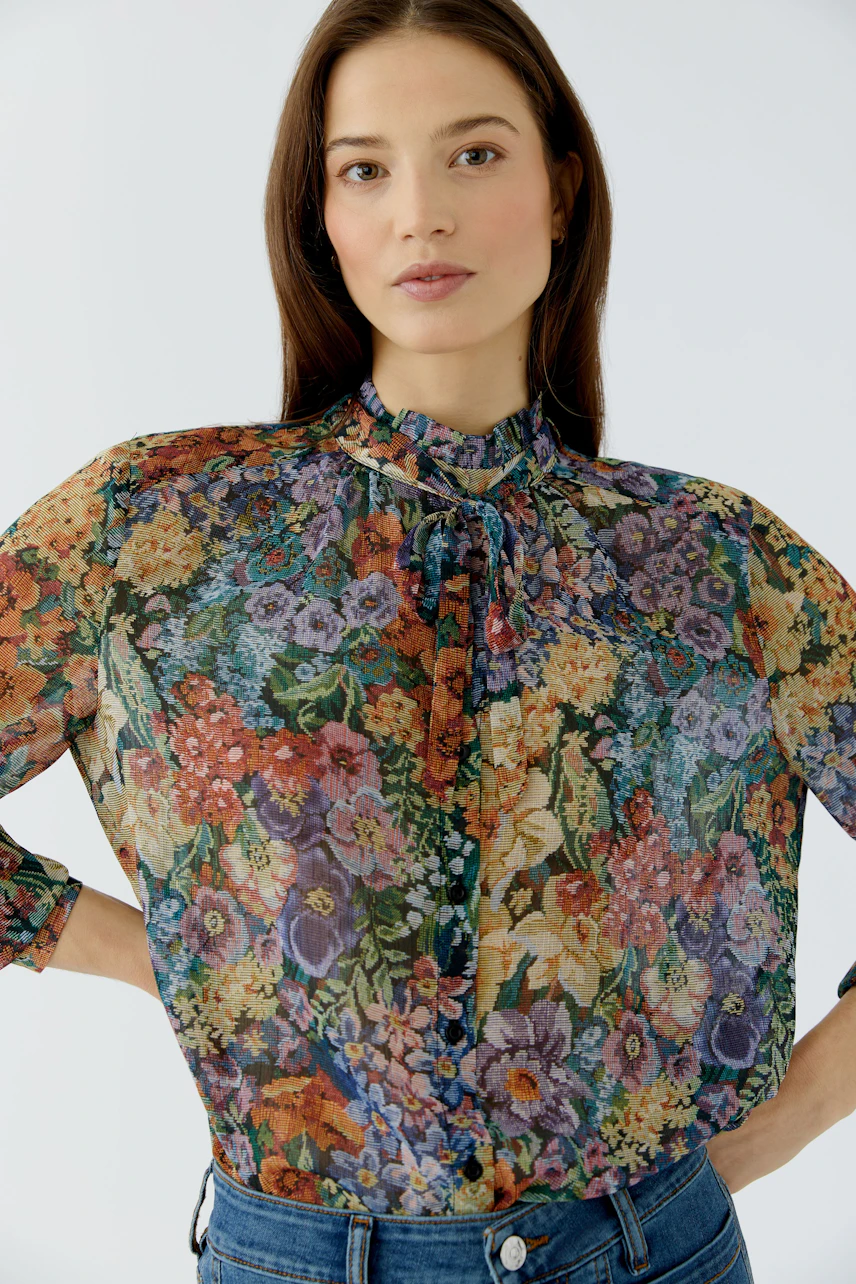 Florale Damen-Bluse: Frau in bunter Bluse mit Blumenmuster und Schleife, kombiniert mit blauer Jeans.