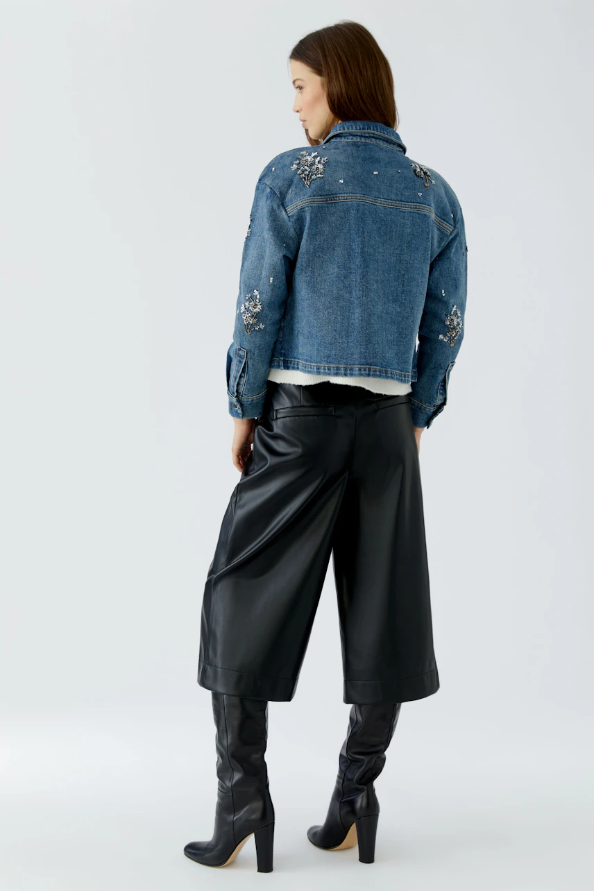 Denim jacket: Woman in a blue jeans jacket with floral embellishments, paired with black culottes and boots.