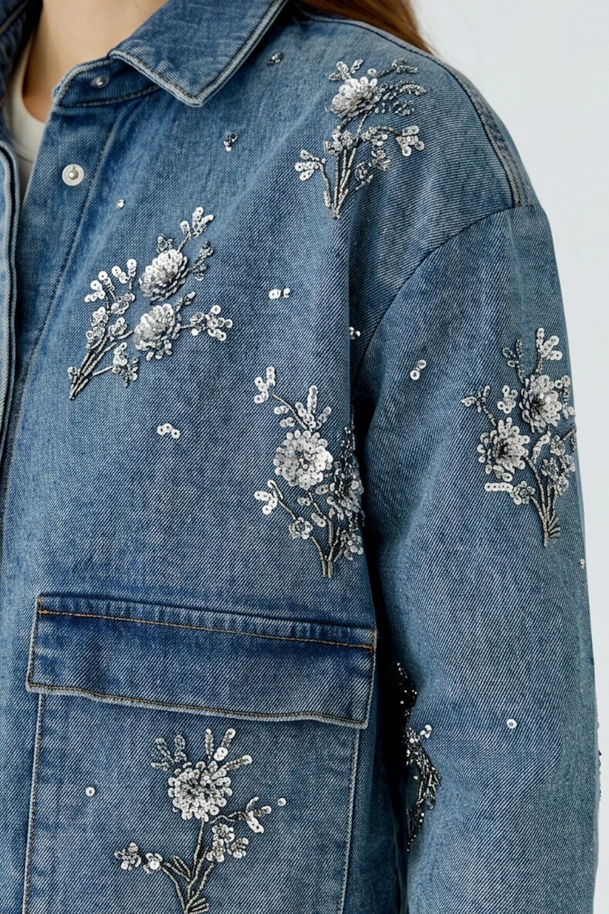 Denim jacket with floral embroidery: Woman in a blue jeans jacket adorned with white floral patterns.