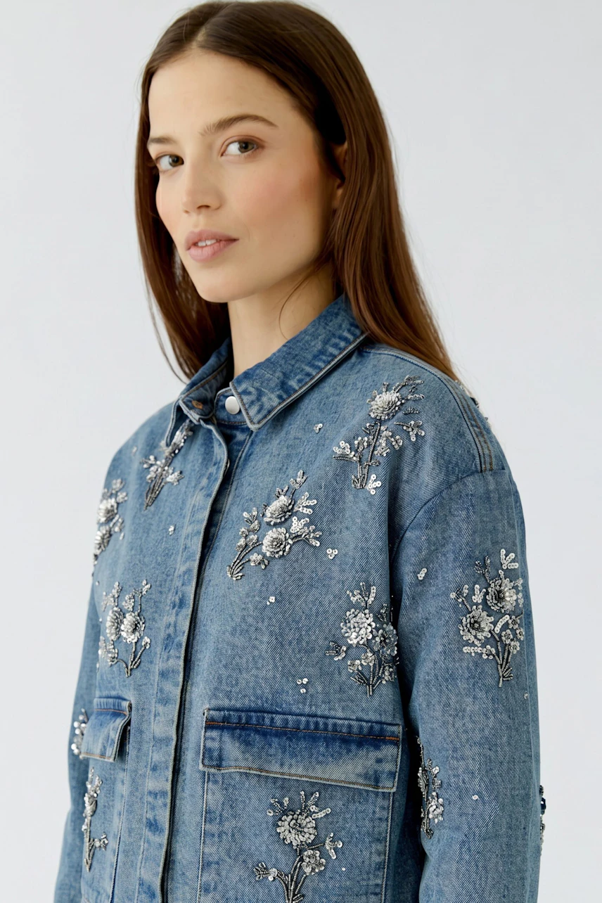 Woman in denim jacket with floral embroidery, looking confidently. Casual and stylish design.