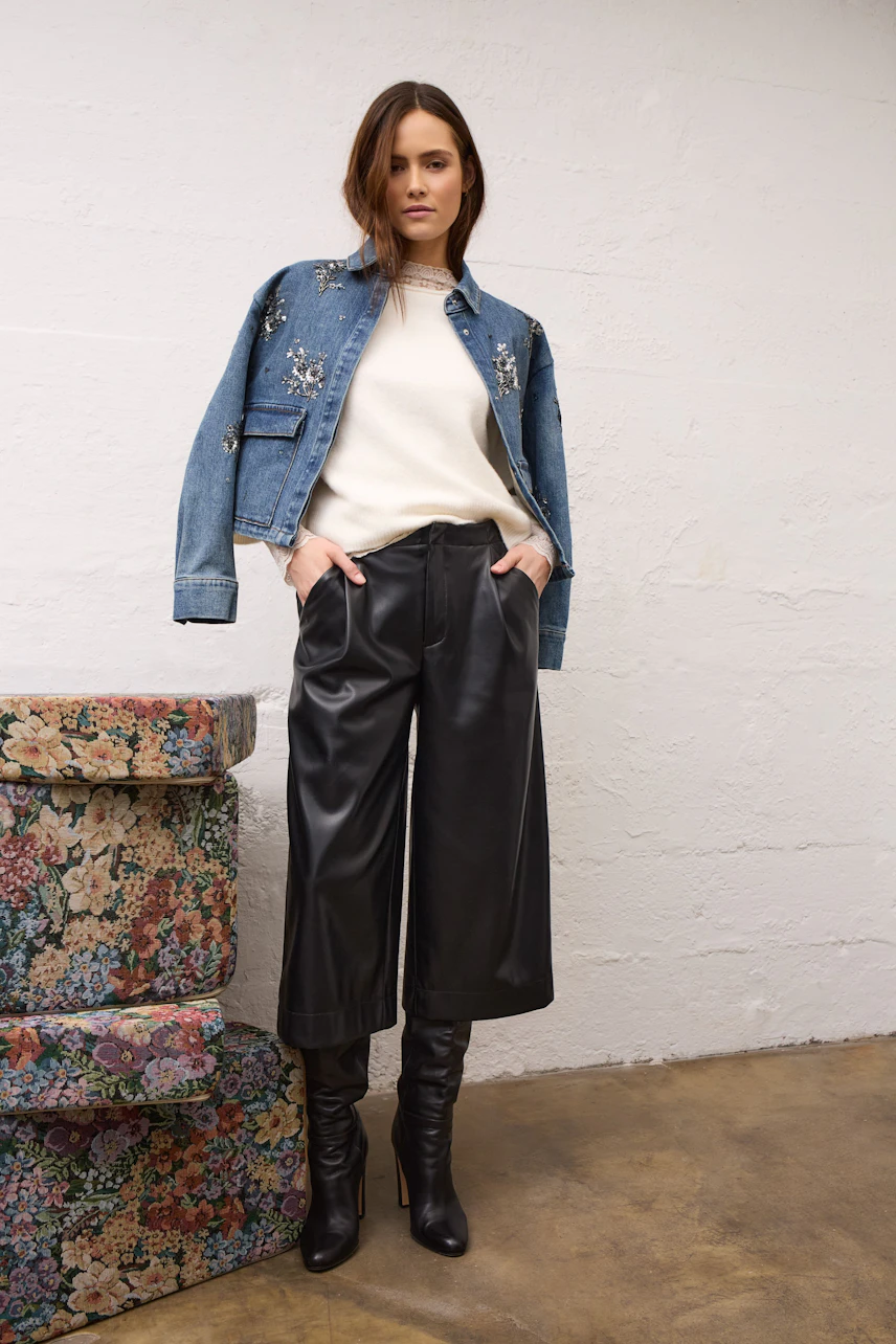 Casual denim jacket: Woman in a blue jeans jacket with floral embroidery, white pullover, and black leather pants.