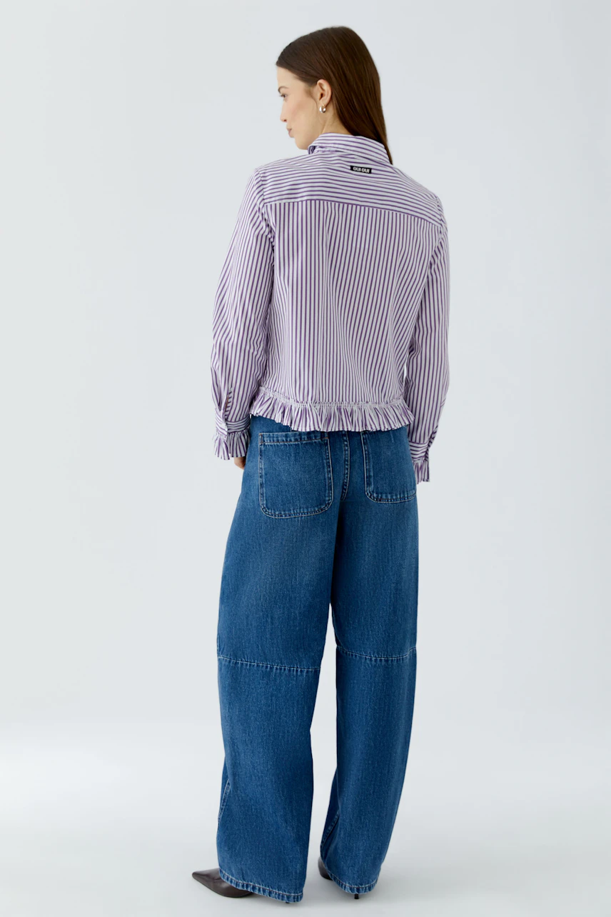 Gestreifte Hemdbluse: Frau in lila-weiß gestreifter Bluse und blauen Jeans, lässig und modern.