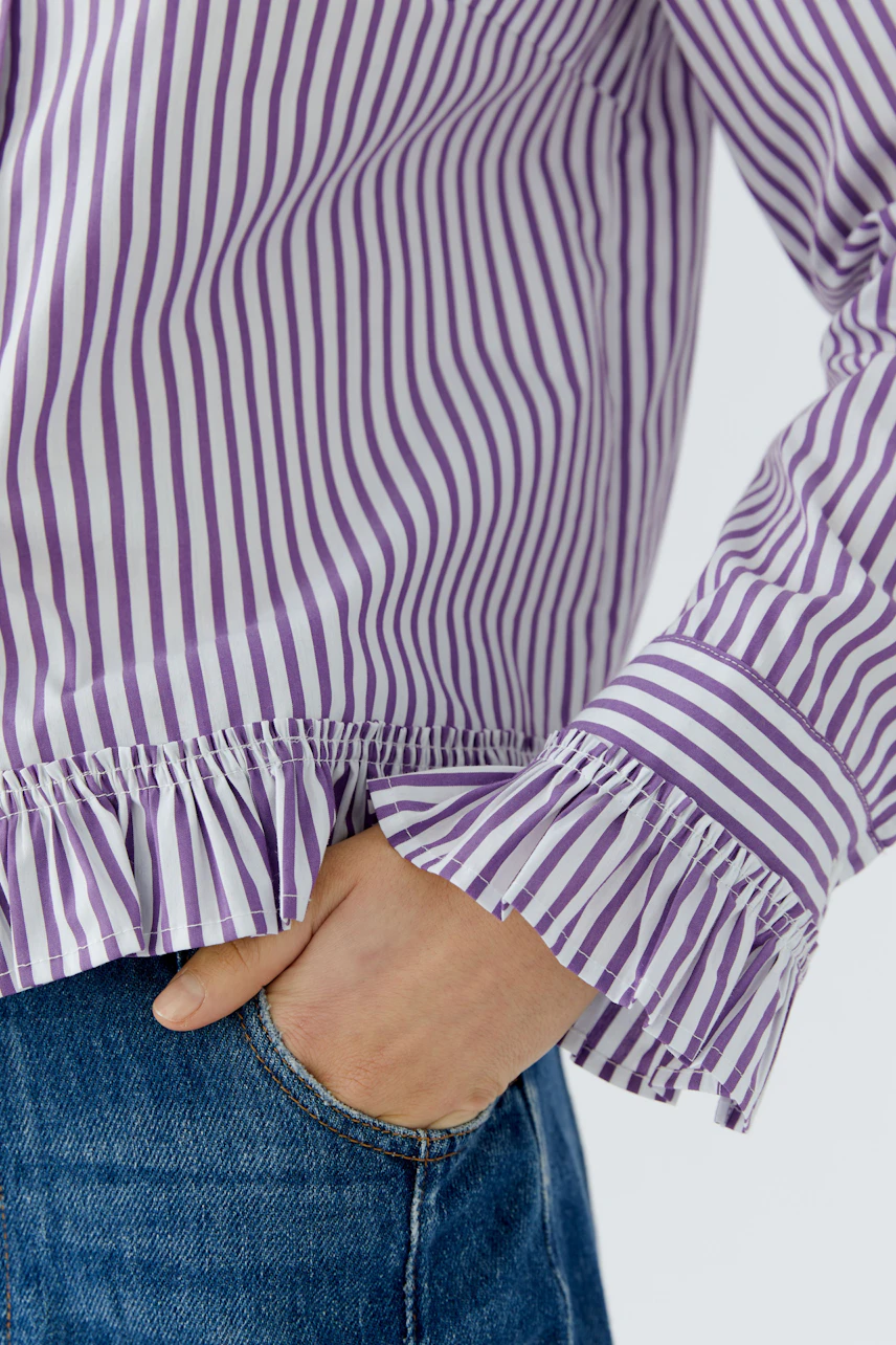 Gestreifte Hemdbluse: Lila-weiße Streifen mit Rüschenärmeln, kombiniert mit blauer Jeans.