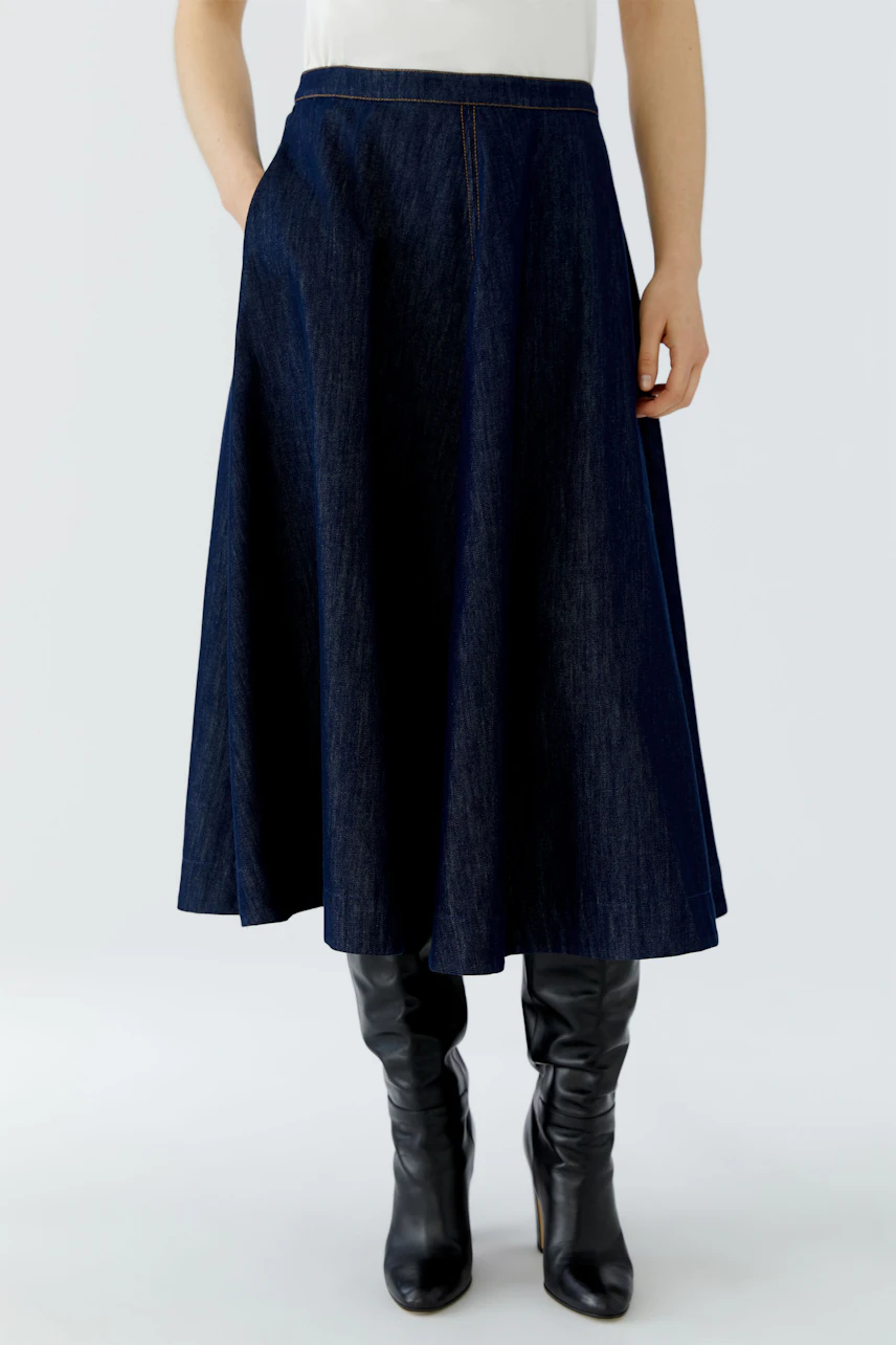 A-line skirt: Woman in a dark denim A-line skirt with black boots, standing confidently.