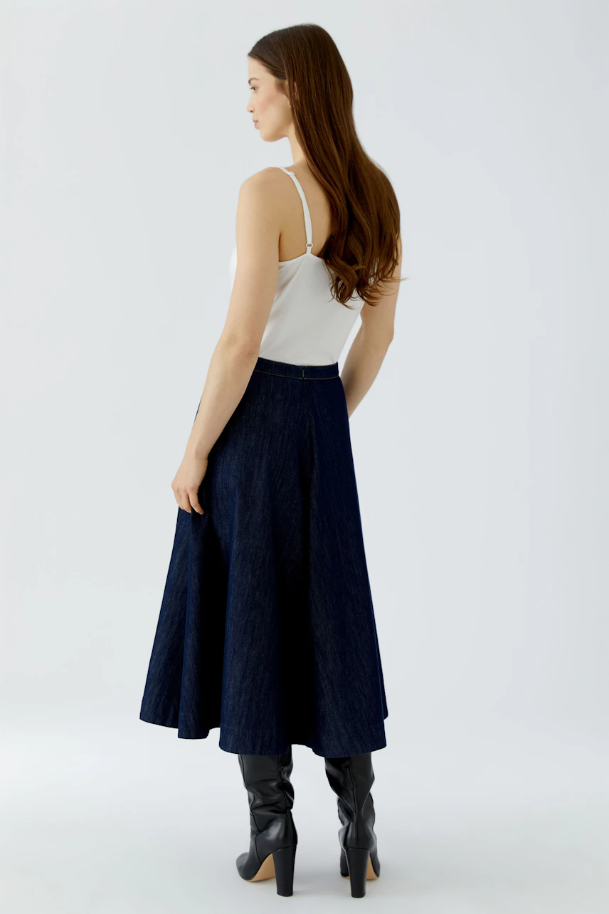 A-line skirt: Woman in a white top and navy A-line skirt with black boots, showcasing a casual style.