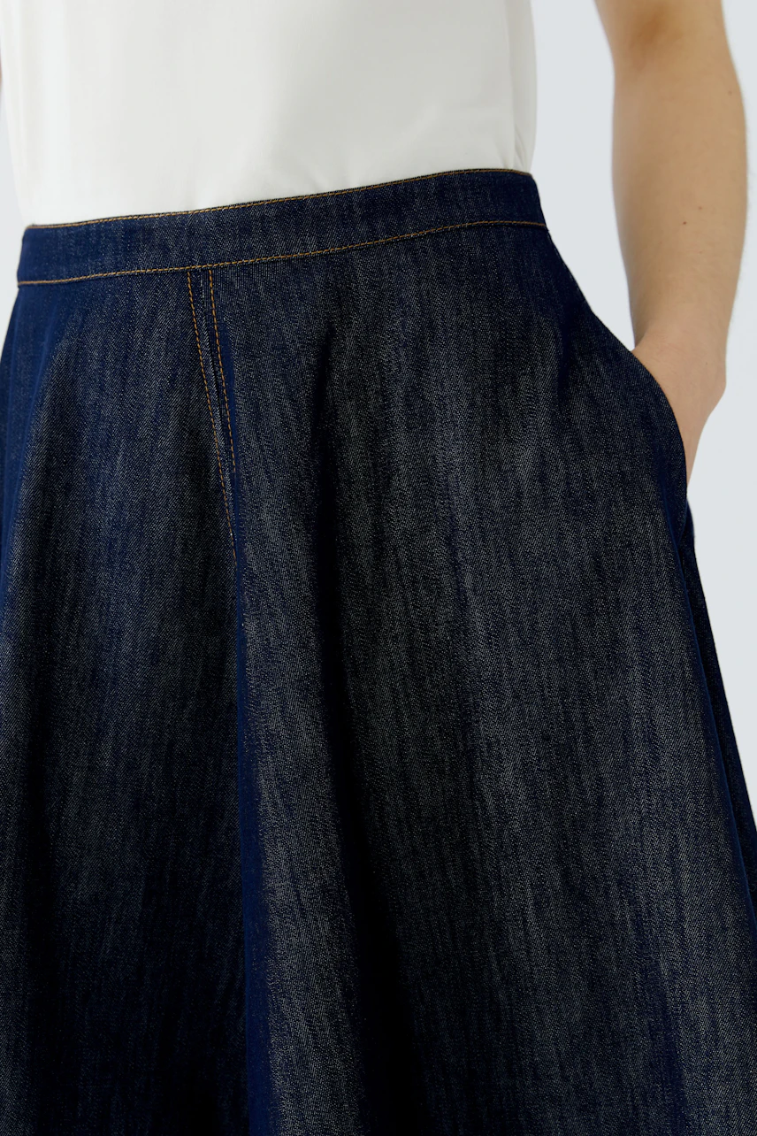 A-line skirt: Woman in a dark denim A-line skirt with a white top, hand in pocket.