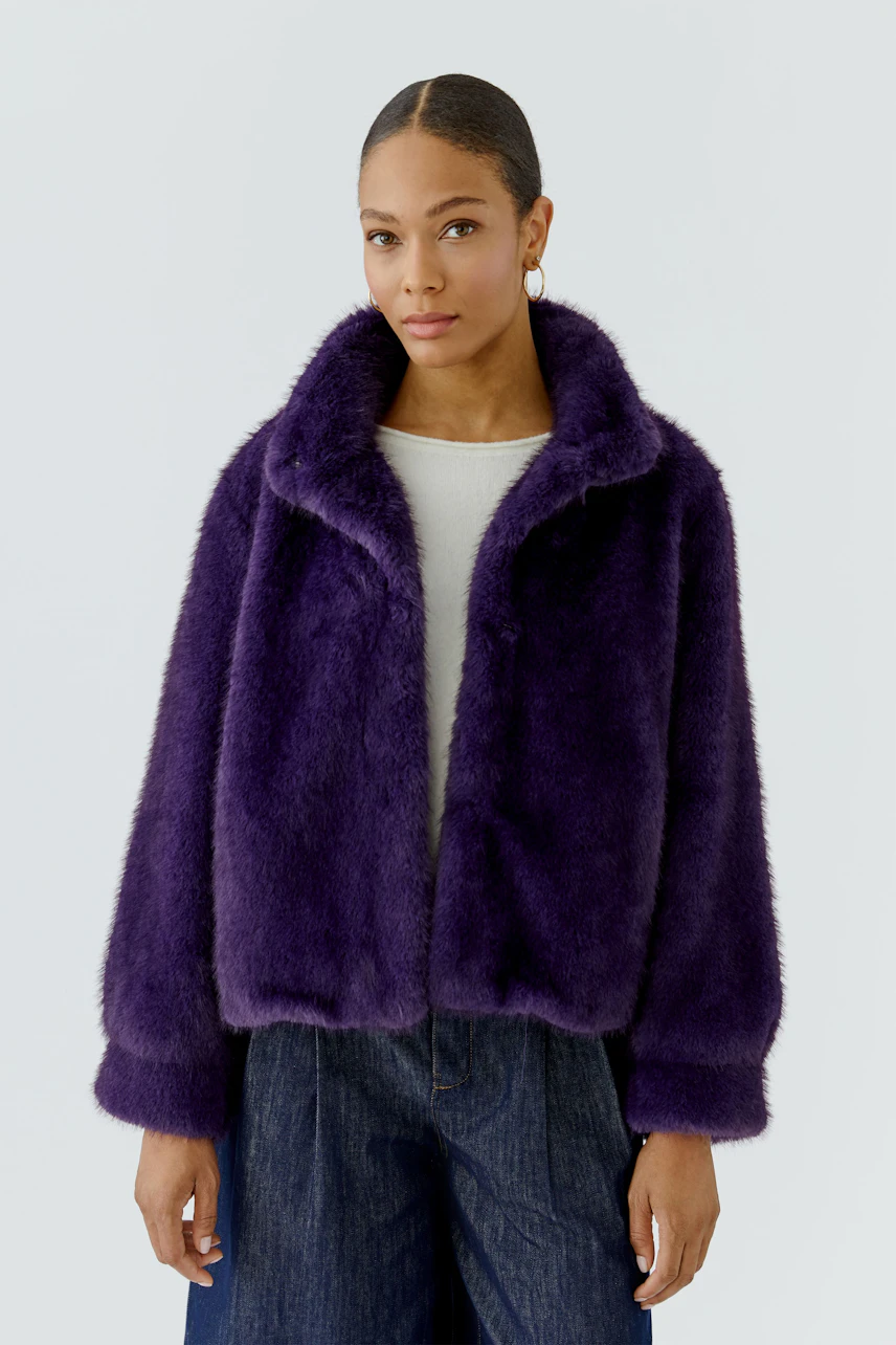 Woman in a purple outdoor jacket, white top, and jeans, looking confidently ahead.