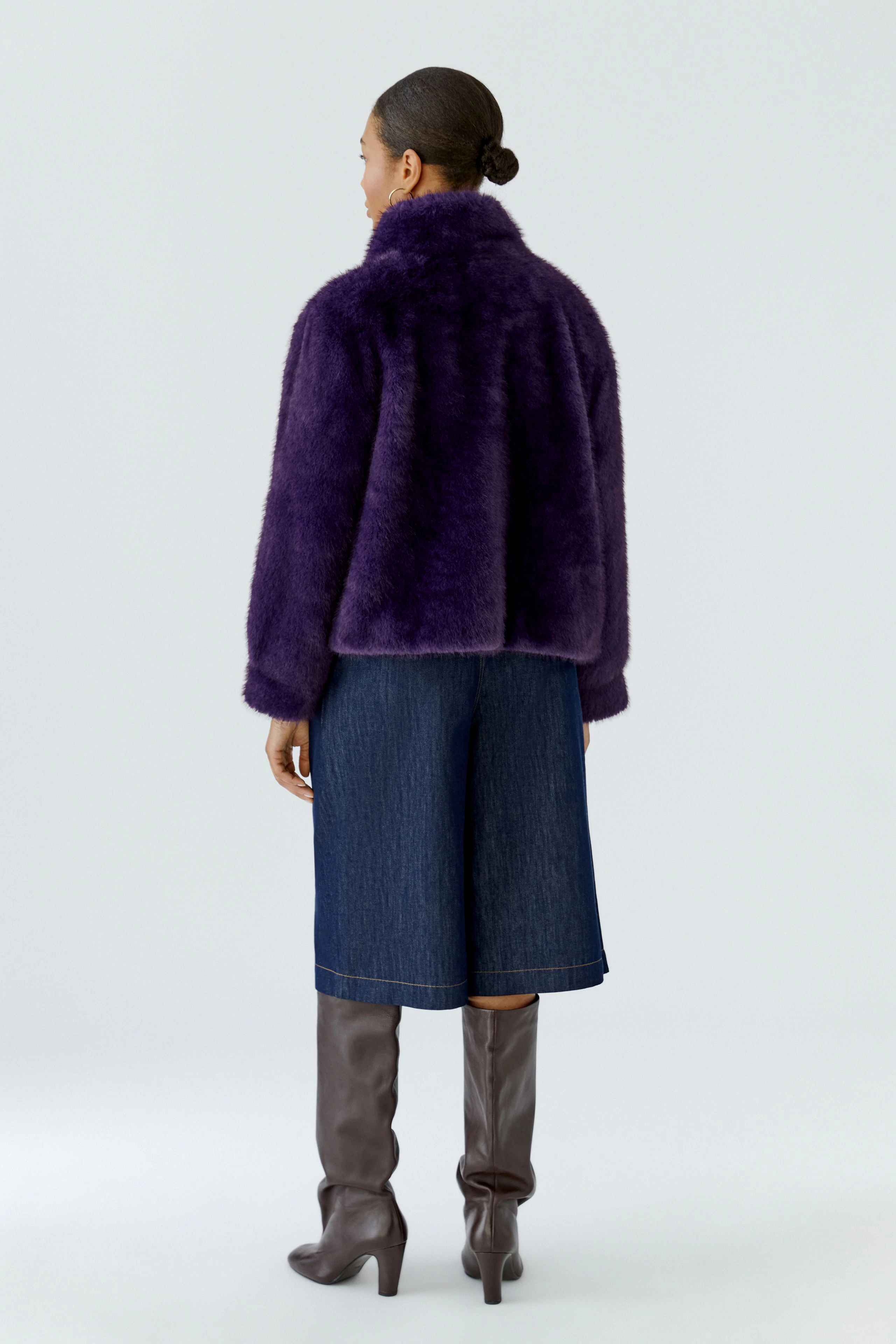 Frau in lila Outdoorjacke, kombiniert mit Jeansrock und braunen Stiefeln. Rückenansicht.