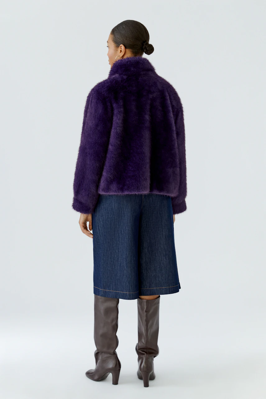 Woman in purple outdoor jacket, denim culottes, and knee-high boots, showcasing a stylish winter look.