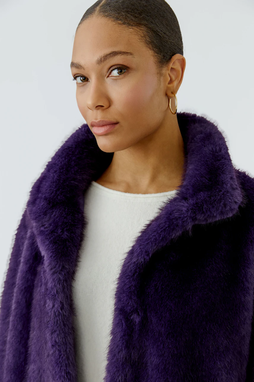 Woman in a purple outdoor jacket, soft texture, over a white top, looking confidently.