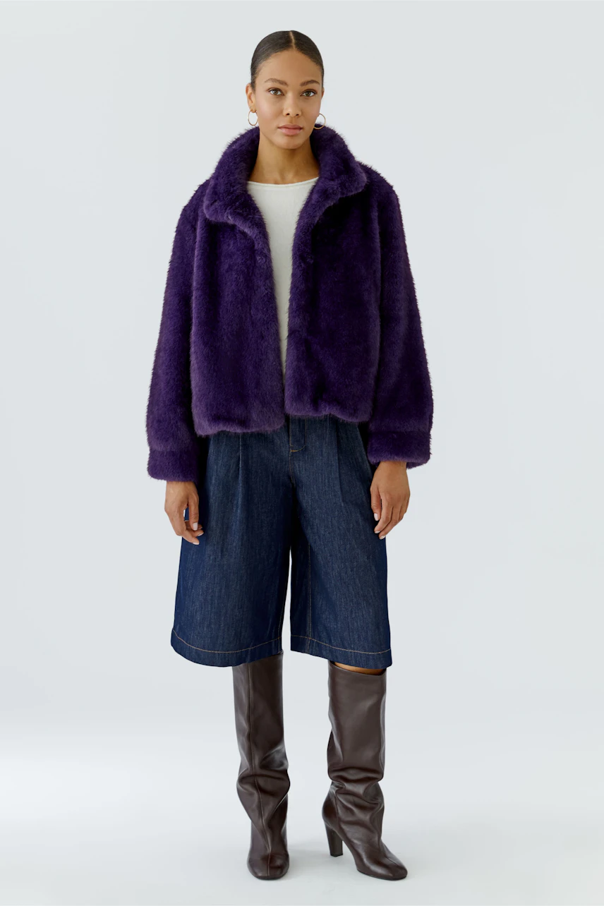 Woman in purple outdoor jacket, white top, denim culottes, and brown knee-high boots.