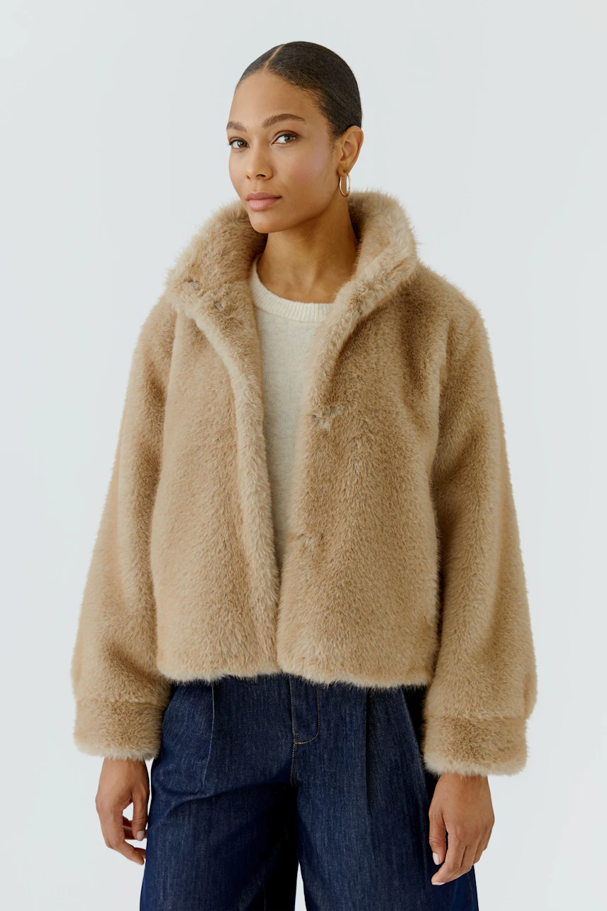 Woman in cozy outdoor jacket: Beige faux fur jacket over cream pullover, paired with dark jeans.