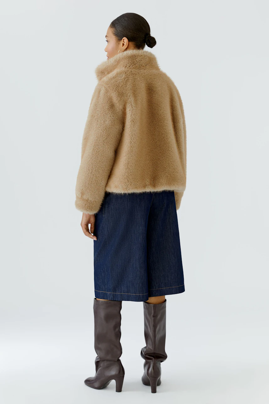 Woman in a cozy outdoor jacket, paired with a denim skirt and tall brown boots, facing away.
