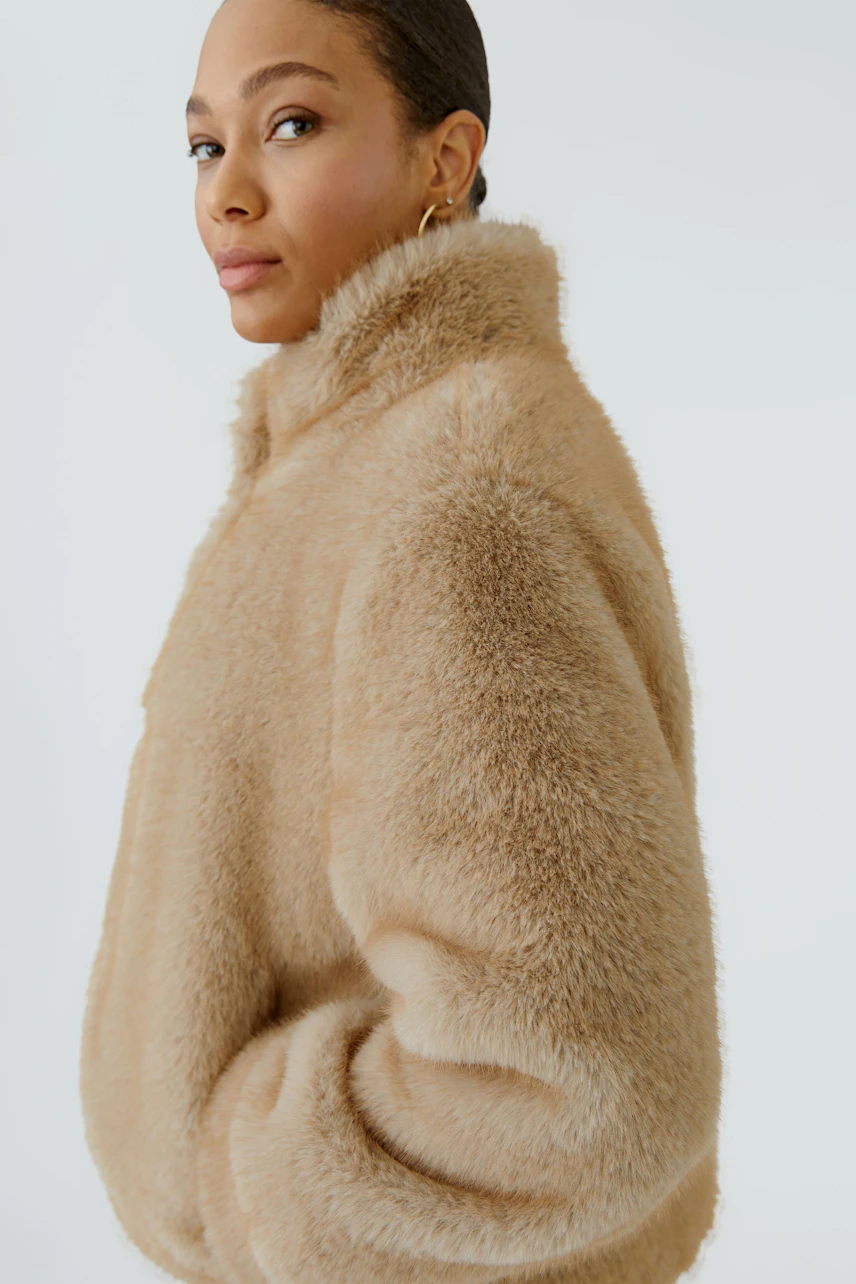Woman in a cozy beige outdoor jacket, looking confidently to the side. Soft texture and warm design.