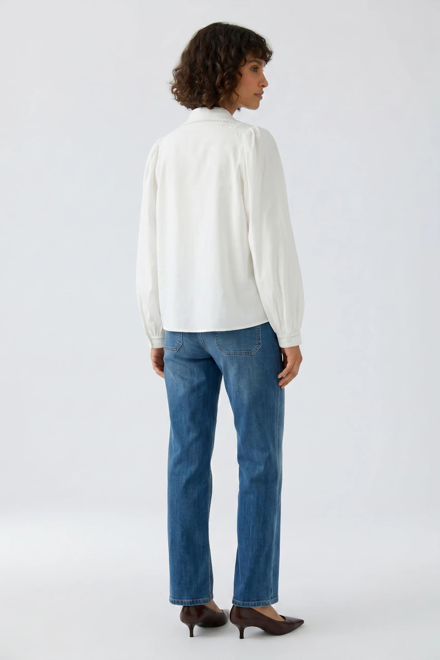 Weiße Bluse: Frau in weißer Bluse und blauer Jeans, von hinten gesehen, mit lockigem Haar.