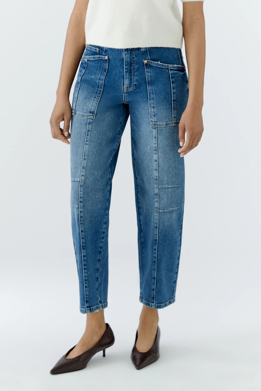 Frau in Jeans Barrel: Lässige, blaue Jeans mit geradem Schnitt und Taschen, kombiniert mit weißen Schuhen.