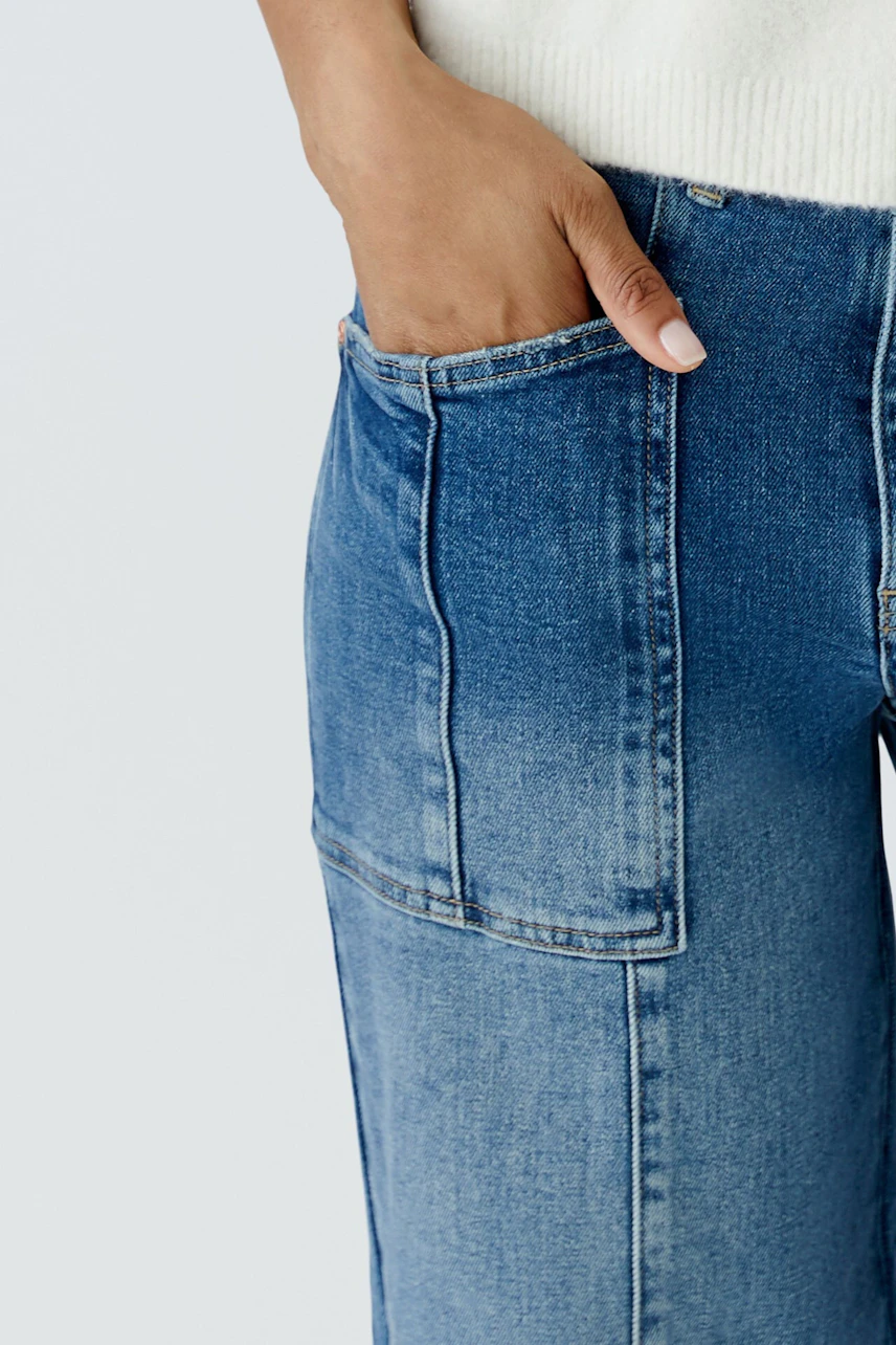 Jeans Barrel: Frau trägt lässige, blaue Jeans mit großen Taschen, kombiniert mit einem weißen Pullover.