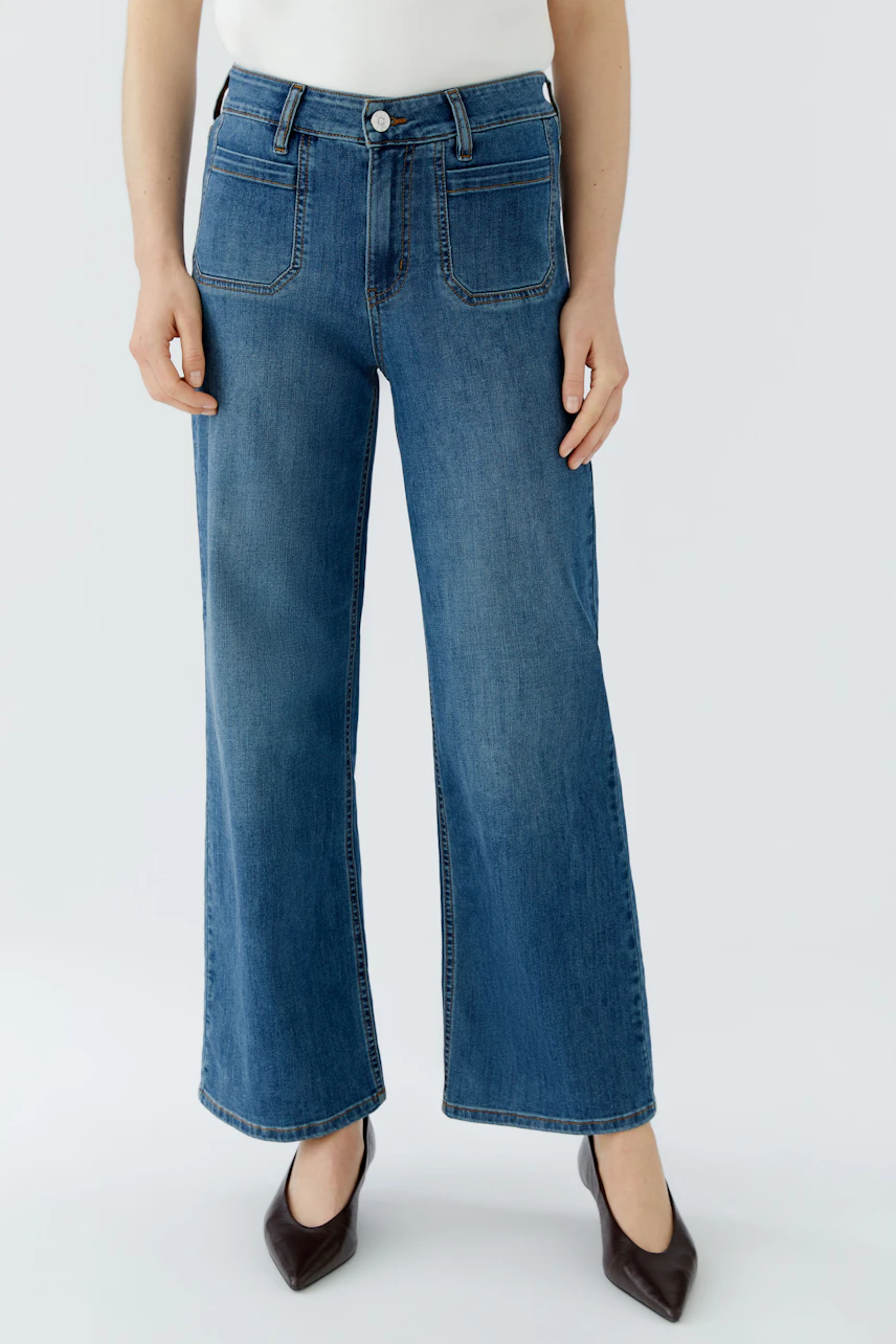 Jeans Straight: Frau in blauer Straight-Jeans, kombiniert mit weißem Top und schwarzen Schuhen.