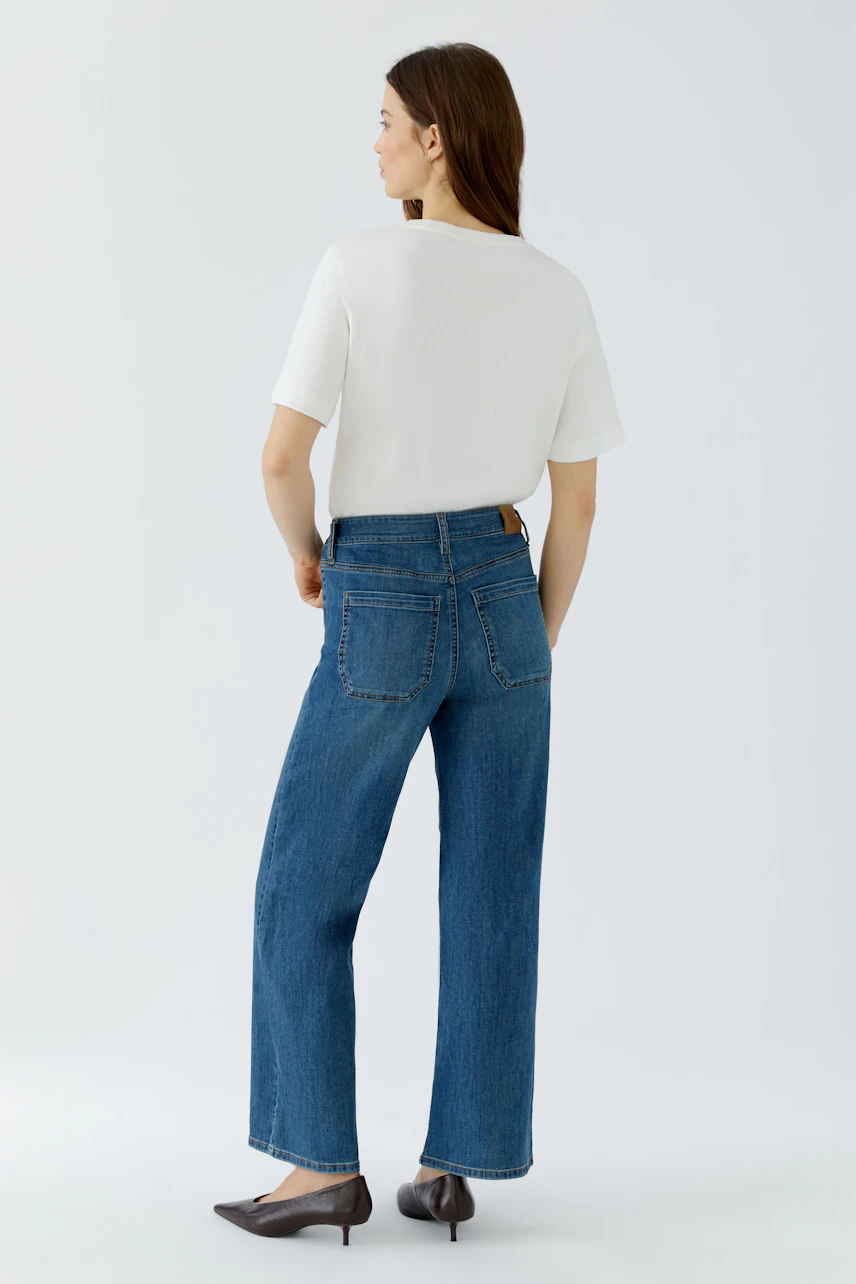 Frau in blauer Jeans Straight und weißem Shirt, von hinten. Lässiger Look mit weitem Bein und Taschen.