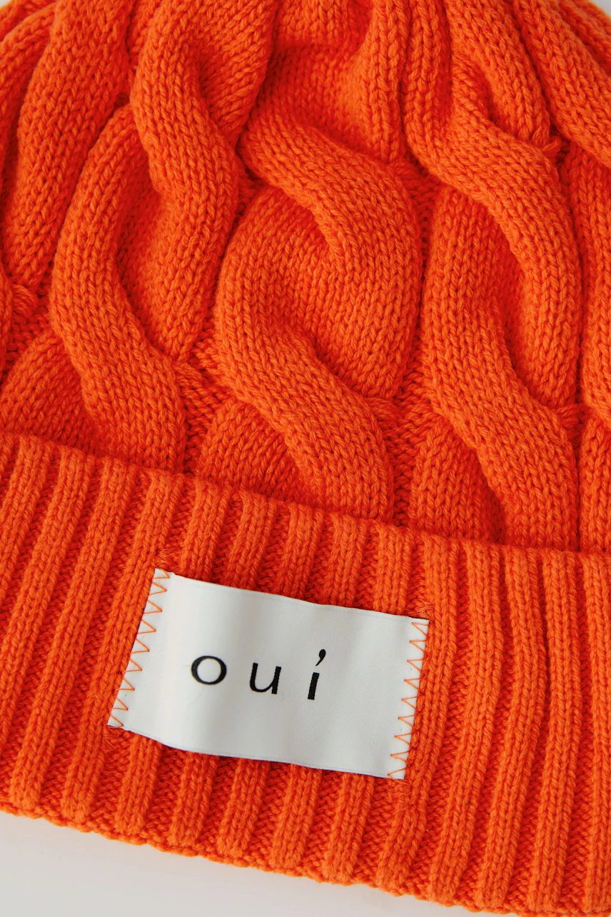 Strickmütze in leuchtendem Orange mit Zopfmuster und Oui-Logo, ideal für kalte Tage.