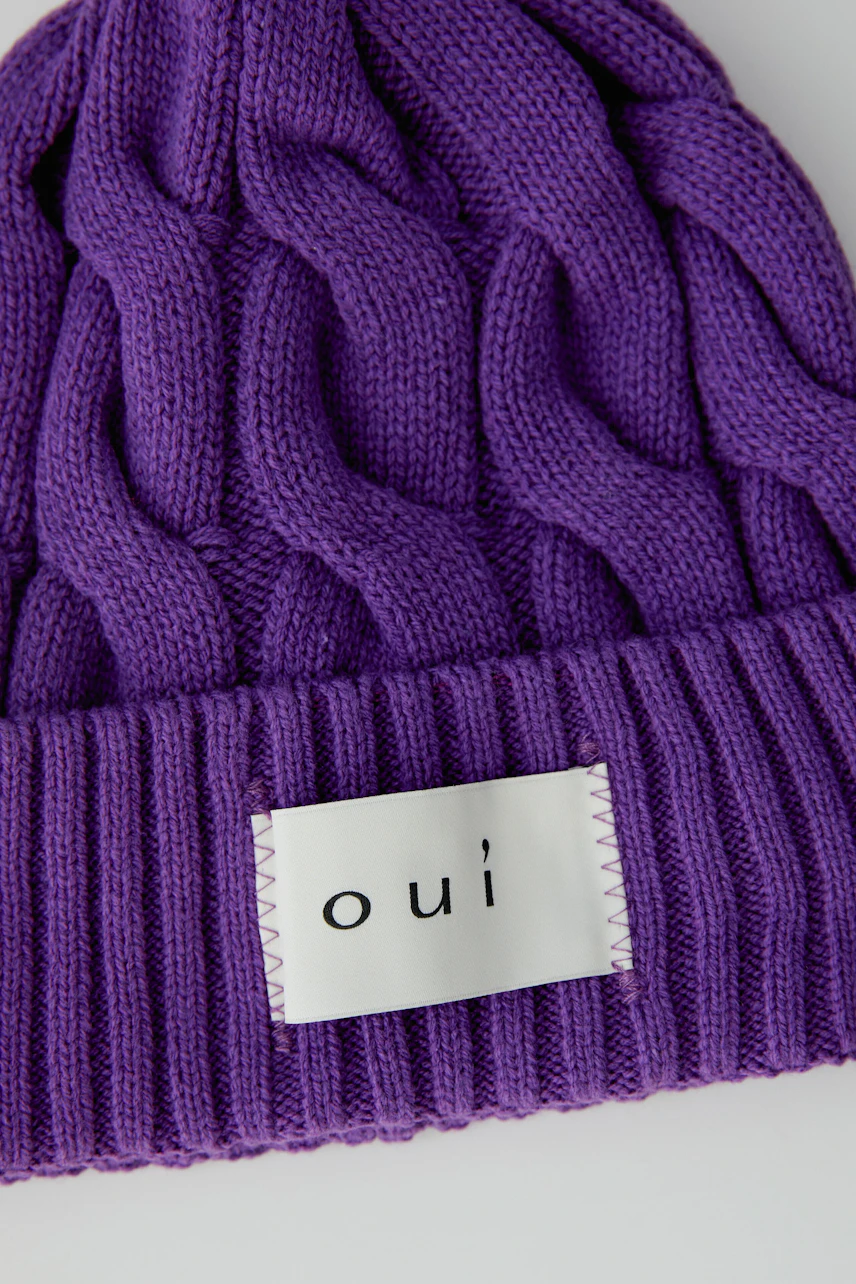 Lila Mütze mit Zopfmuster und Oui-Logo, ideal für kalte Tage. Weiches Material für angenehmen Tragekomfort.
